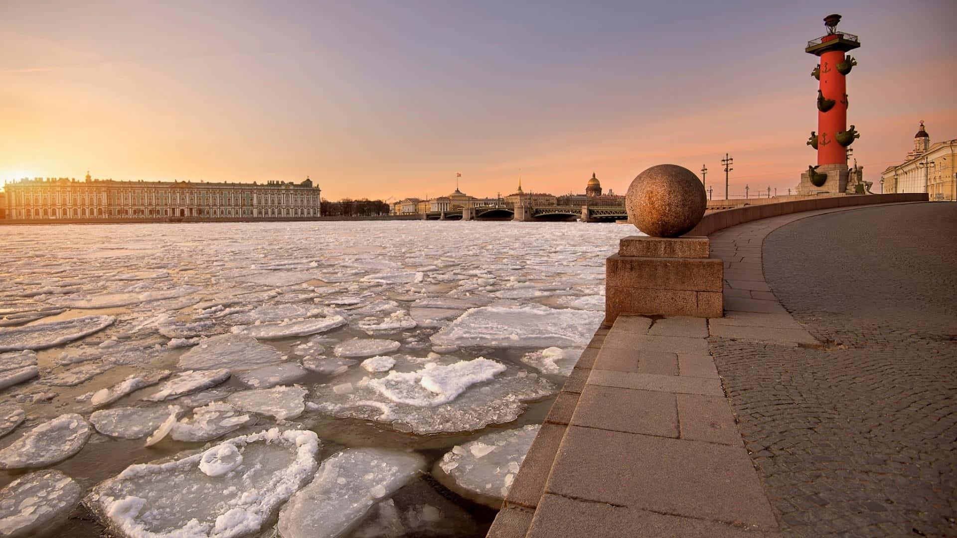 Russia 桌布 壁紙 — 夕陽照耀著聖彼得堡結冰的河流，河上有浮冰，由石欄杆和標誌性的紅色亞歷山大柱框住。