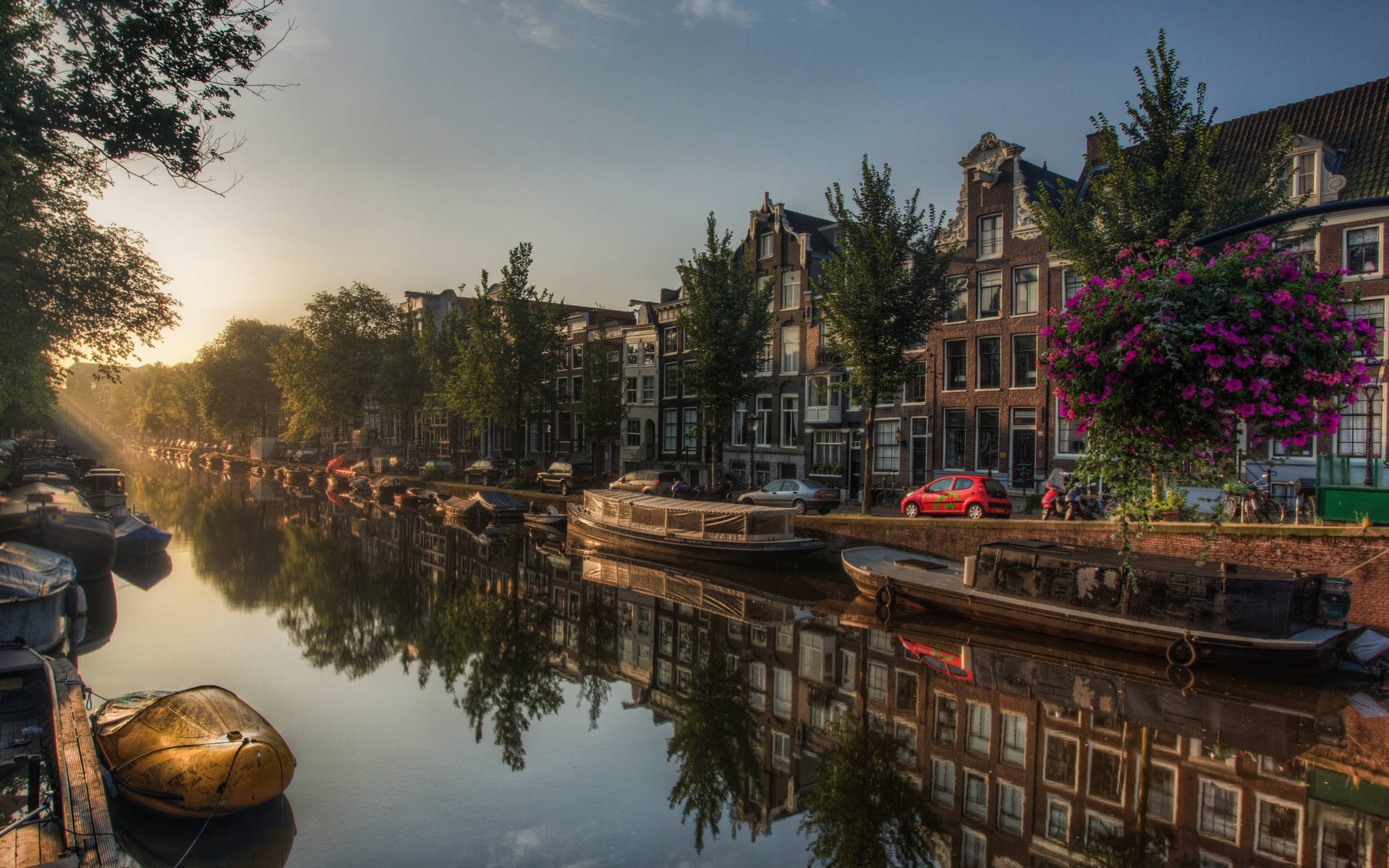 Netherlands 桌布 壁紙 — 夕陽照耀著阿姆斯特丹運河，歷史悠久的山牆房屋和停泊的船隻在平靜的水面上倒映。