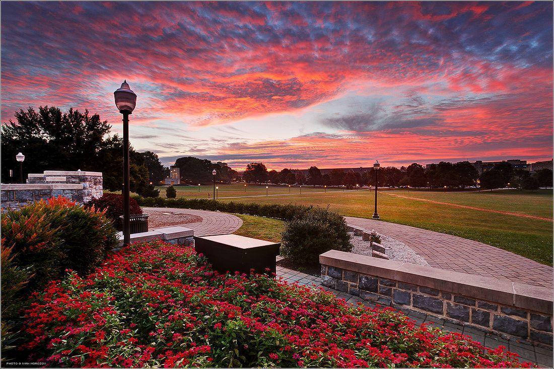 Virginia Tech 桌布 壁紙 — 夕陽燦爛，將公園上方的天空染成火紅和紫色，公園內有石徑和盛開的紅花。