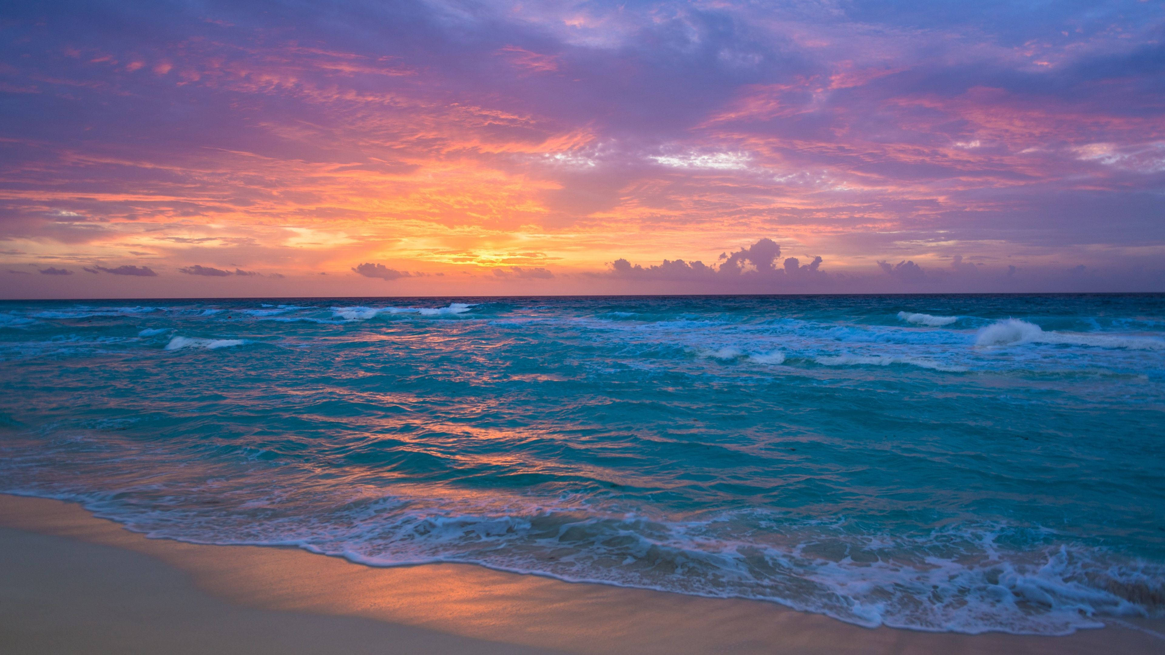 海洋 桌布 壁紙 — 夕陽燦爛，將天空染成火熱的橙色和紫色，海浪拍打著金色的沙灘。