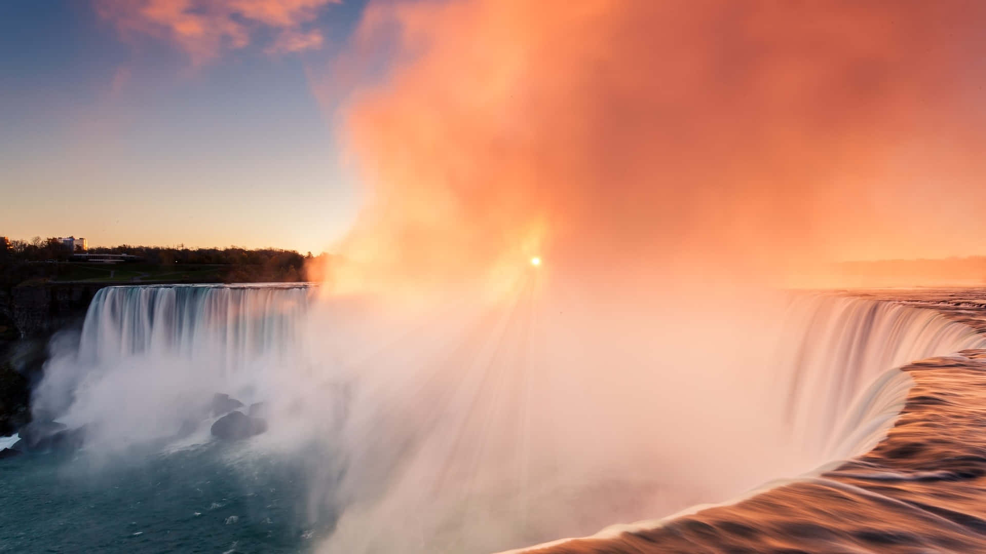 Niagara Falls Canada 桌布 壁紙 — 夕陽的光線穿透從巨大瀑布升起的薄霧，瀑布散發著溫暖的橙色和藍色色調。