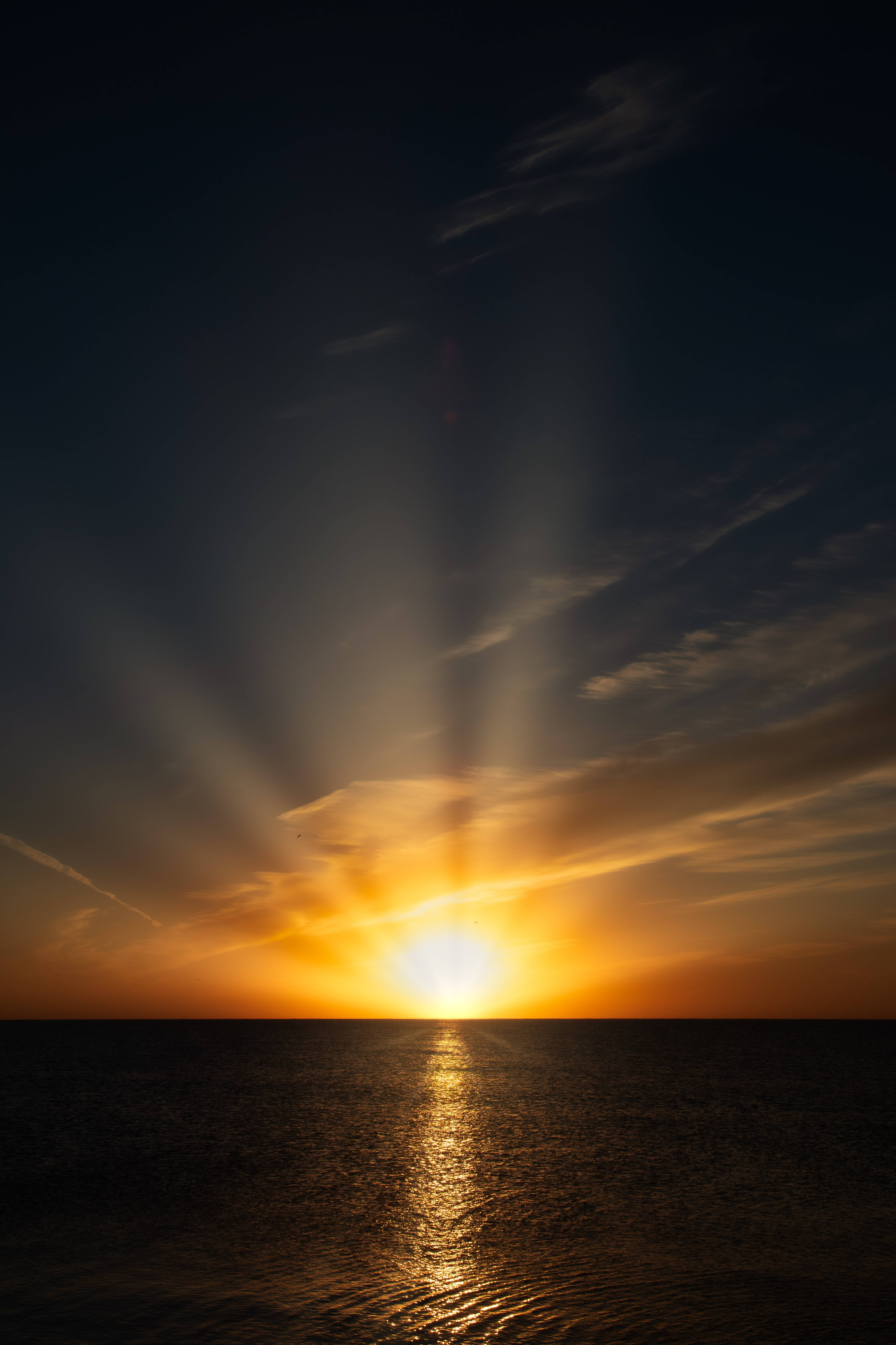 日出 桌布 壁紙 — 夕陽的光芒穿透烏雲，映照在平靜的海面上，形成金色的倒影。