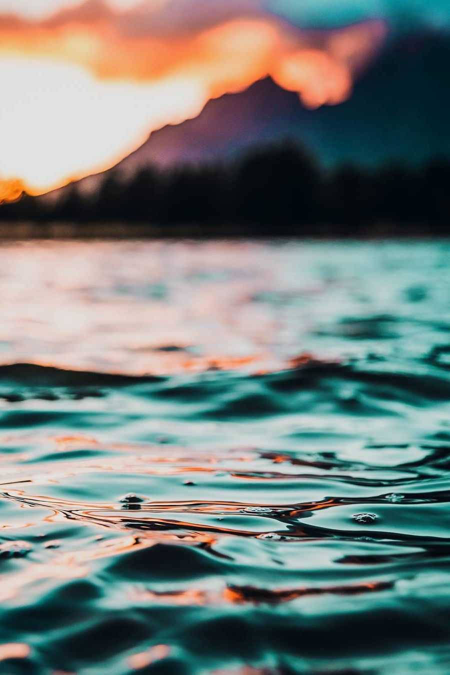 海洋 桌布 壁紙 — 夕陽的色彩在平靜的湖面上泛起漣漪，遠山在火紅的天空中映襯出剪影。