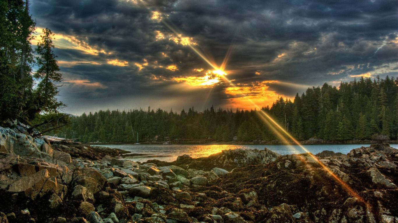 自然 桌布 壁紙 — 夕陽穿透暴風雲層，照射在岩石湖泊上，周圍是茂密的松樹林。