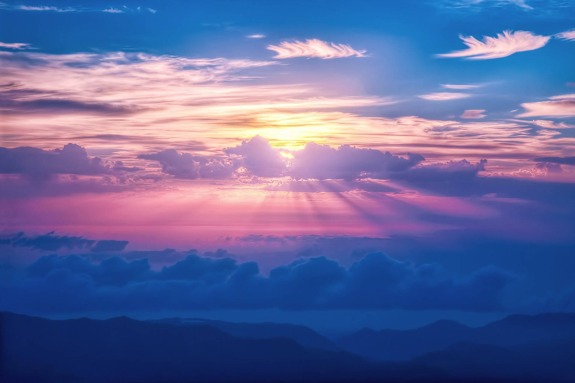 美學雲朵 桌布 壁紙 — 夕陽穿透粉紅、紫色和藍色的雲層，照射在層層疊疊的山巒剪影之上。