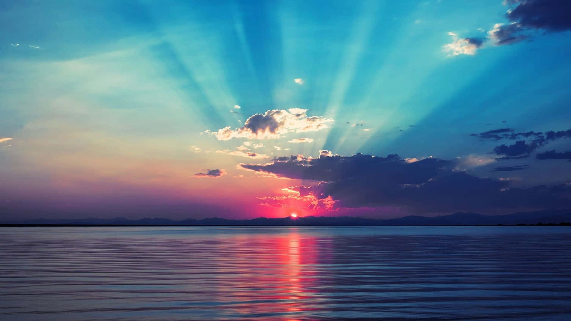 Sunrise Desktop 桌布 壁紙 — 夕陽穿透雲層，映照在平靜的湖面上，反射出火紅的粉紅和藍色天空。