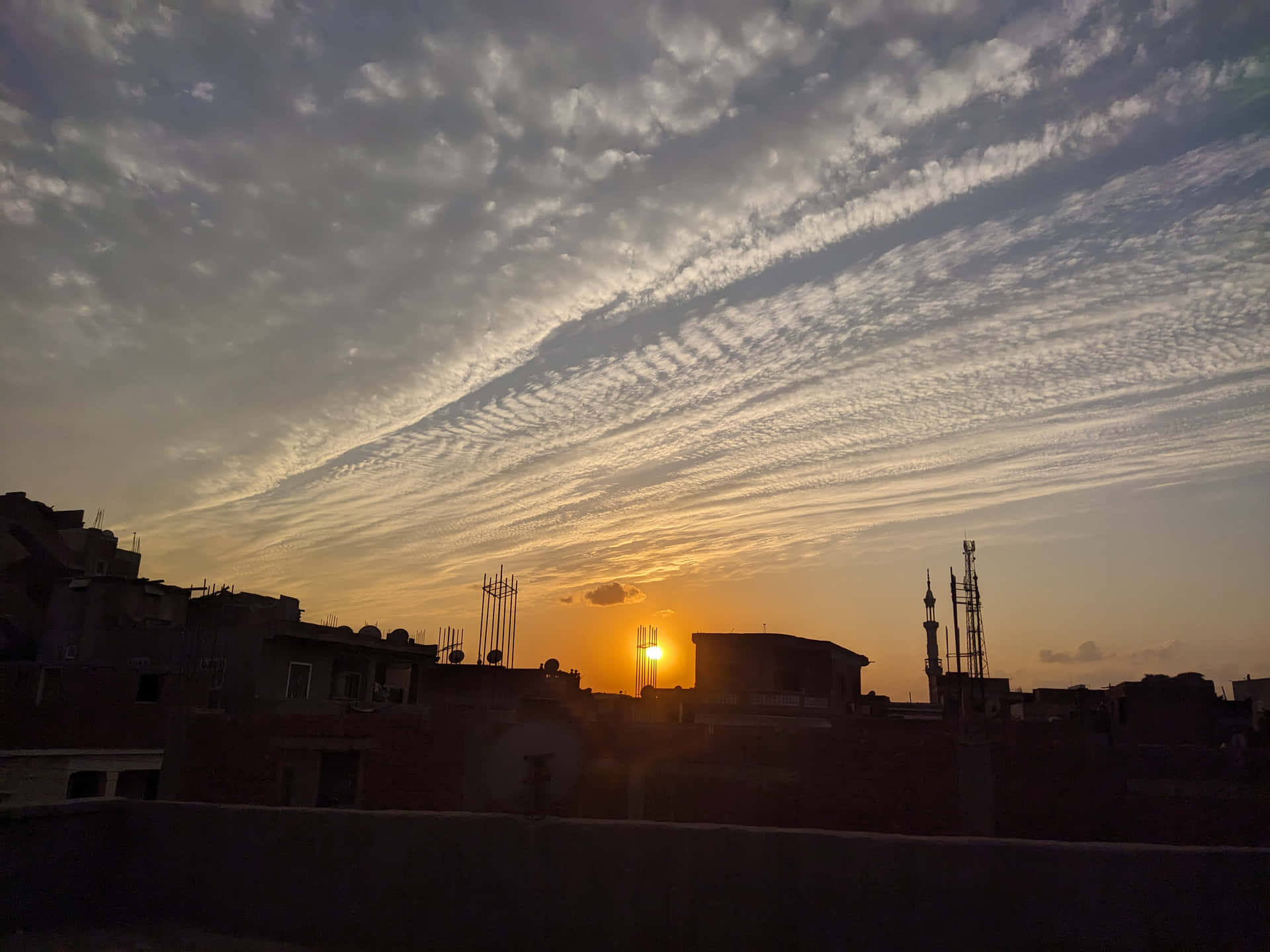 wallpaper 壁紙 — 夕陽穿過縷縷薄雲，將金色光芒灑落在城市屋頂和宣禮塔的剪影之上。