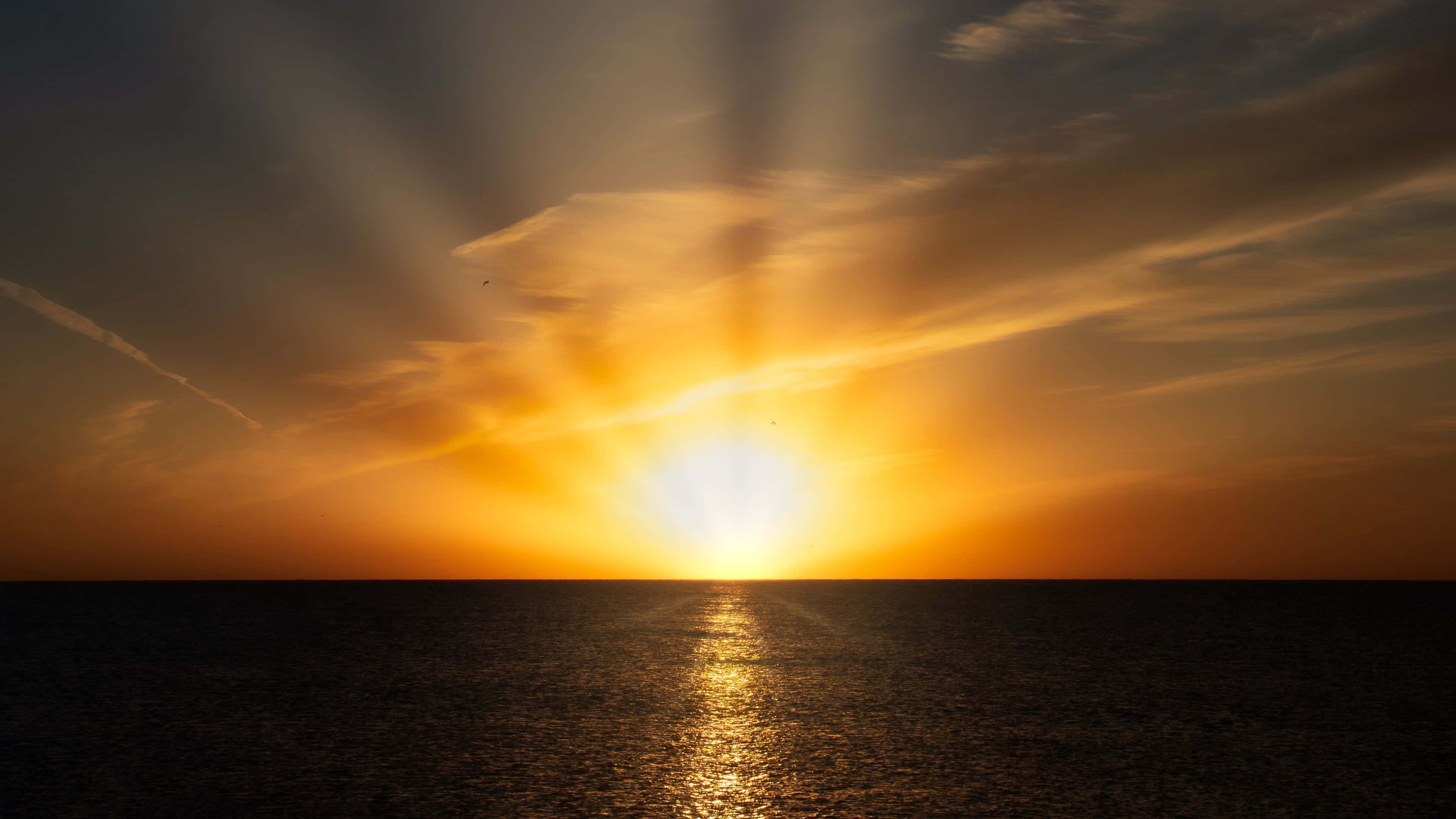 日出 桌布 壁紙 — 夕陽穿過雲層，照射在平靜的海面上，反射出金色的光芒。