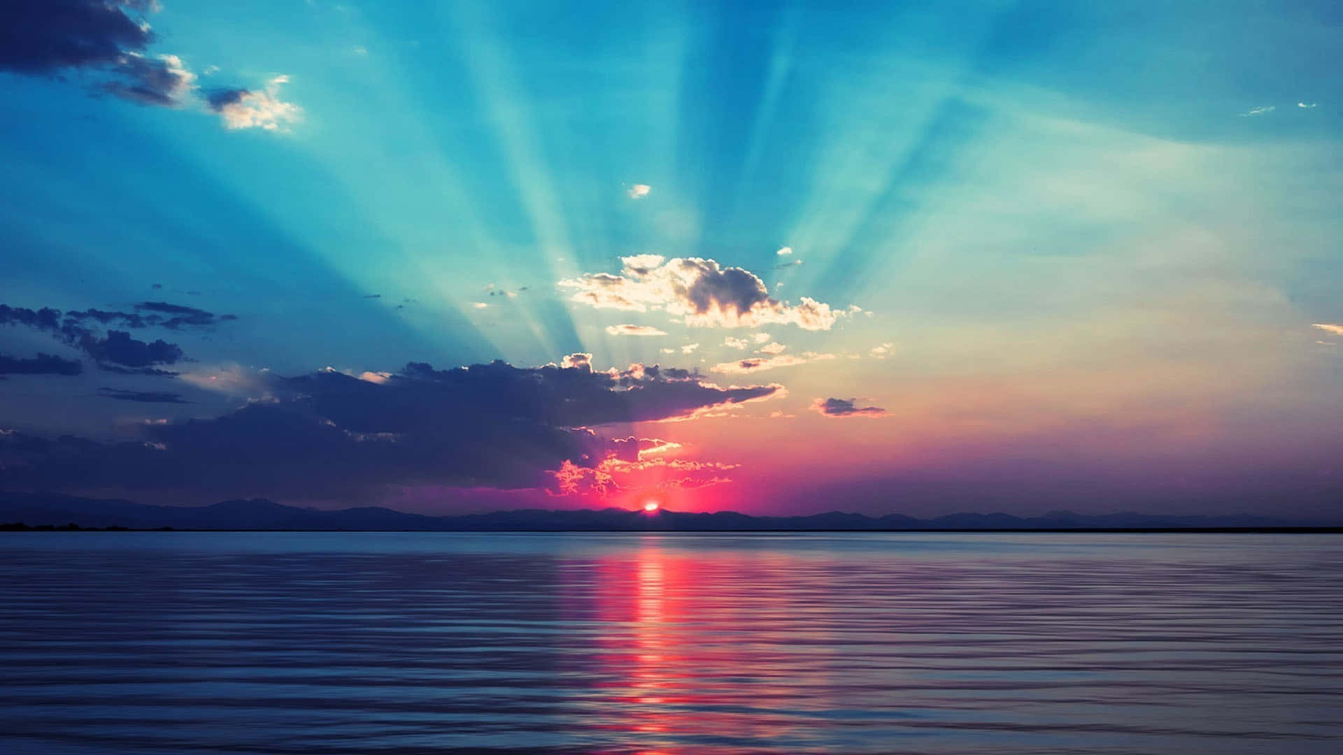 Calm 桌布 壁紙 — 夕陽穿過雲層，照射在平靜的湖面上，反射出火紅的粉紅和藍色天空。