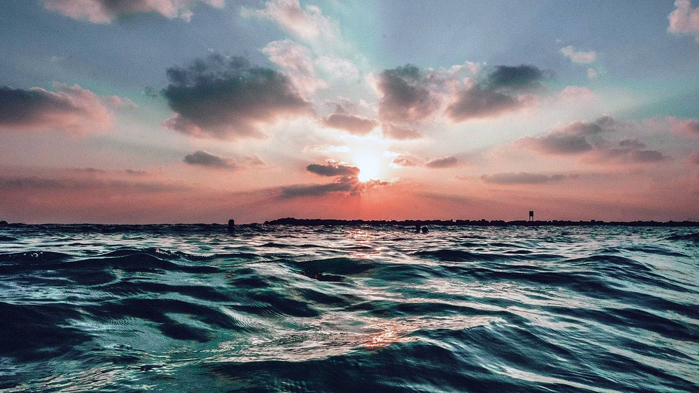 Morning 桌布 壁紙 — 夕陽穿過雲層，照耀在波光粼粼的海面上，遠處有陸地輪廓。