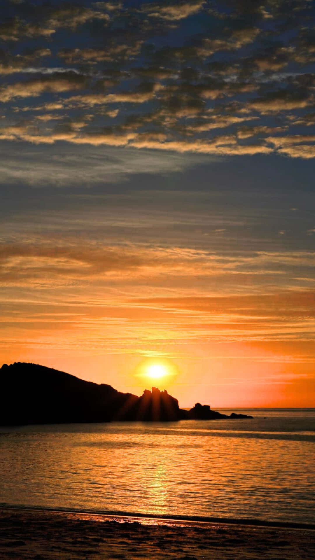 Golden Sunset Over Coastal Rocks and Calm Ocean With Silhouette Shoreline and Reflective Water 壁紙 — 夕陽西下，在平靜的水面上，一輪紅日沉沒在岩石海岸線的剪影之後，將天空染成火紅的橙色和金色。