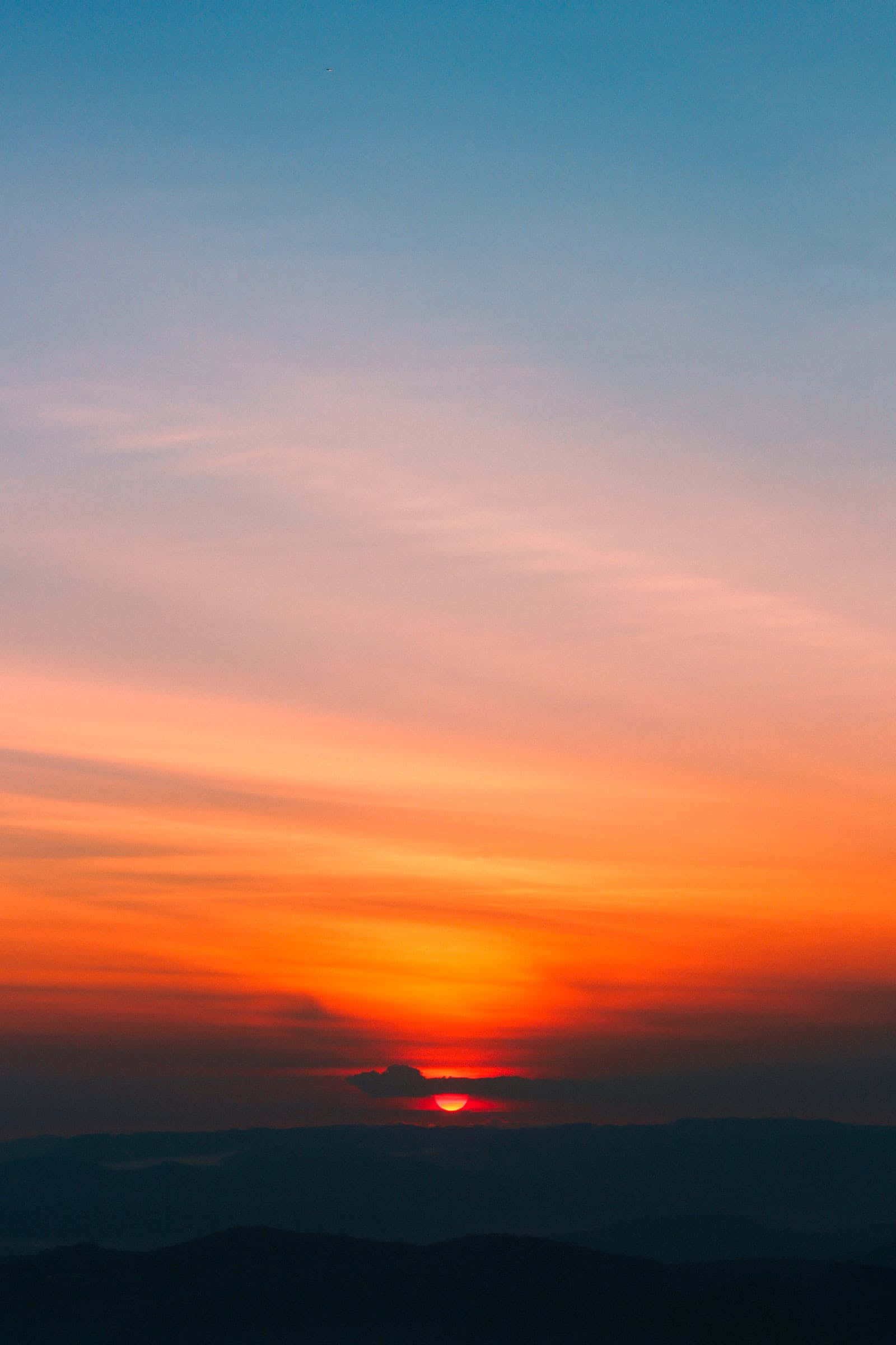 Cute Sunset 桌布 壁紙 — 夕陽西下，在輪廓分明的山脈上空，用火熱的橙色和柔和的粉紅色調描繪天空。