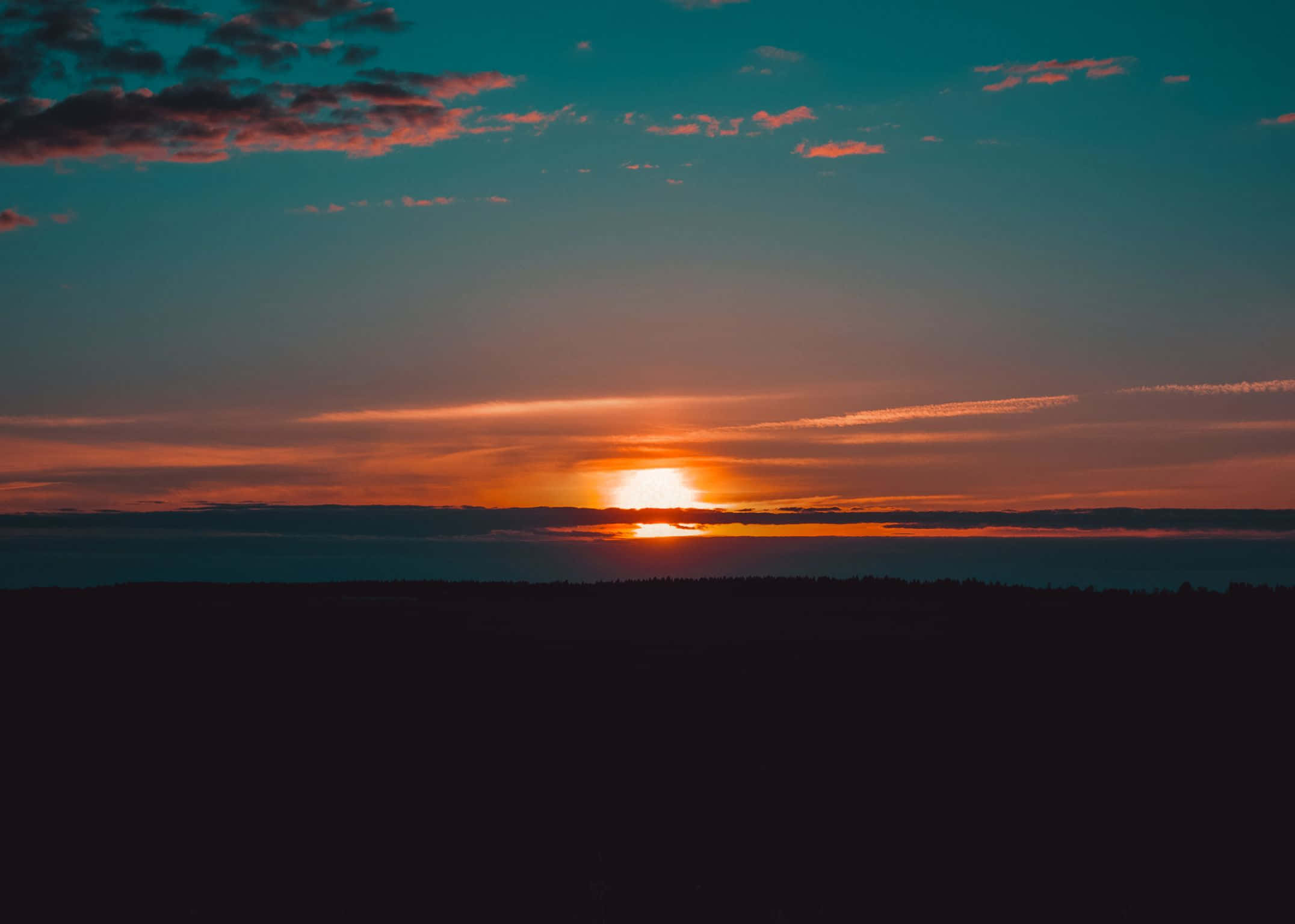 2152x1536 桌布 壁紙 — 夕陽西下，在黑暗森林的輪廓後方，將天空染成火熱的橙色和藍綠色。