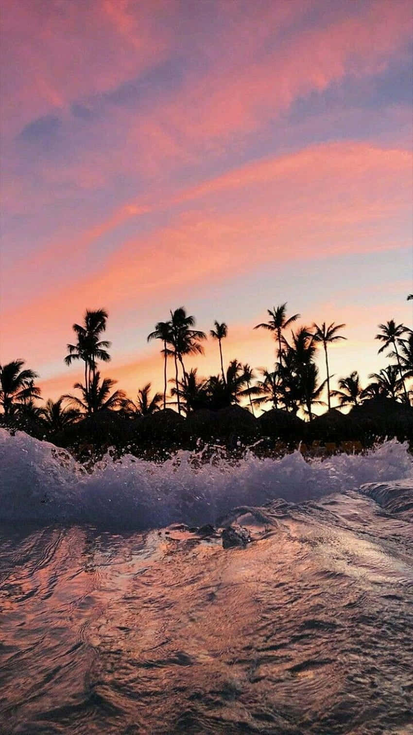 iPhone X Malibu 桌布 壁紙 — 夕陽西下，天空染上粉紅和橙色的鮮豔色彩，襯托著棕櫚樹的剪影和拍岸的海浪。