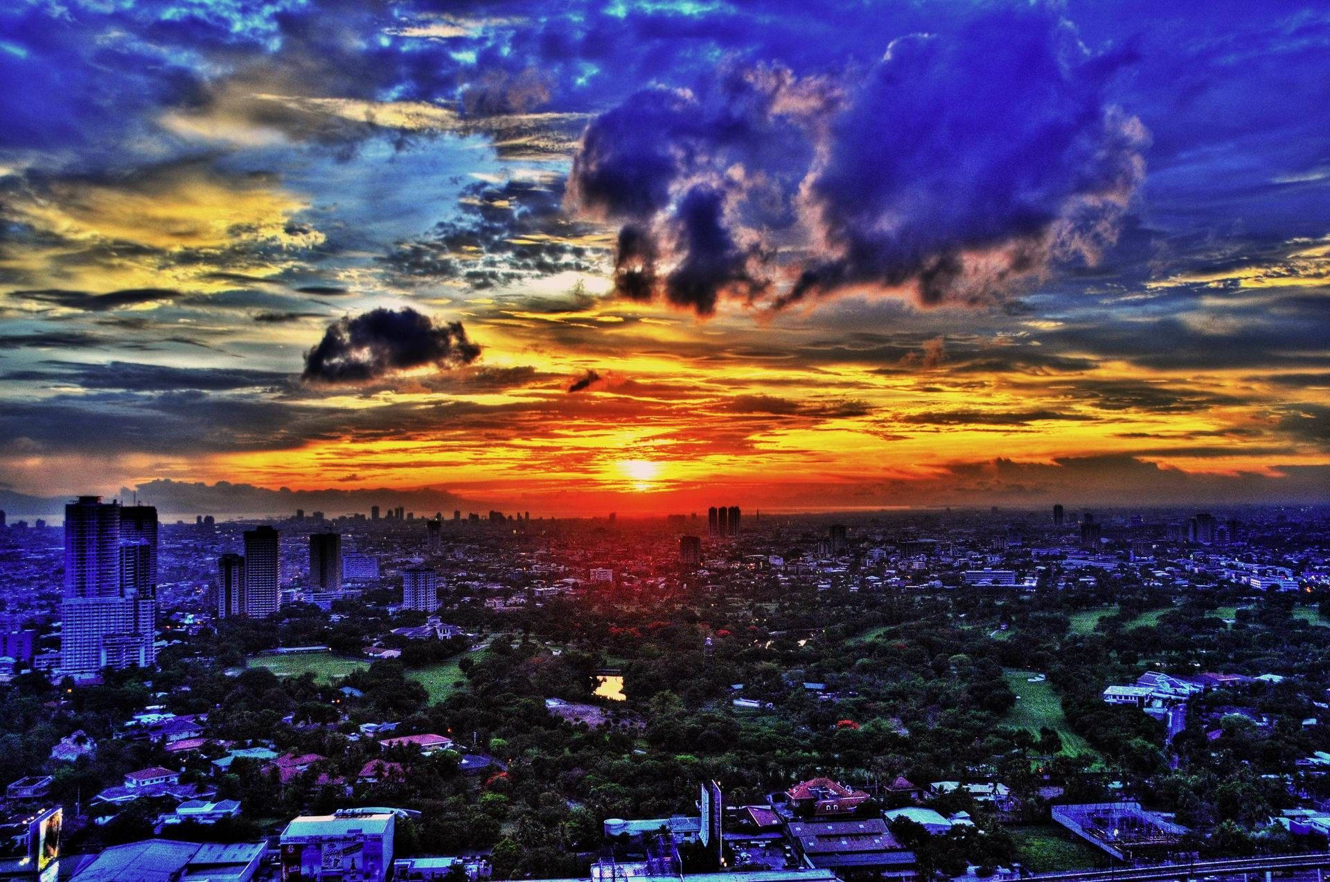 Manila 桌布 壁紙 — 夕陽西下，天空被染成火橙色和深紫色，下方是廣闊的城市景觀，高樓大廈與綠色公園交錯。