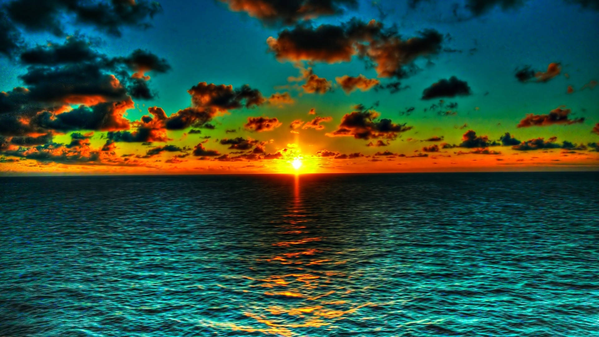 Tumblr Sunset Desktop 桌布 壁紙 — 夕陽西下，海面上呈現出充滿活力的色彩，火紅的太陽在戲劇性的雲層下，在碧綠的海浪上投下金色的倒影。