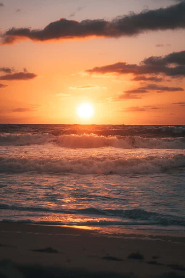 日落 桌布 壁紙 — 夕陽西下，海面上波濤洶湧，拍打著沙灘，天空呈現出火橙色和深紫色的鮮豔色彩。