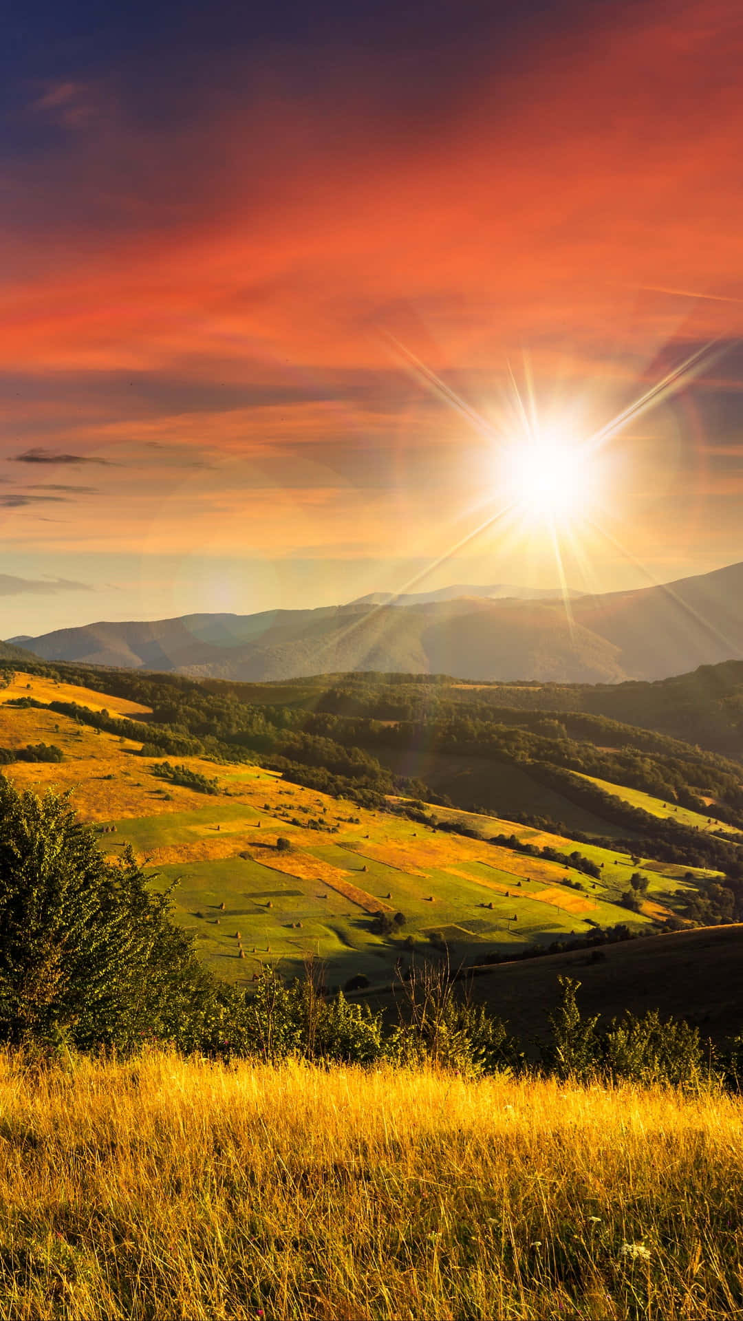 山景 桌布 壁紙 — 夕陽西下，燦爛的陽光穿透火紅色的天空，照耀在起伏的金色山丘和遠山之上。