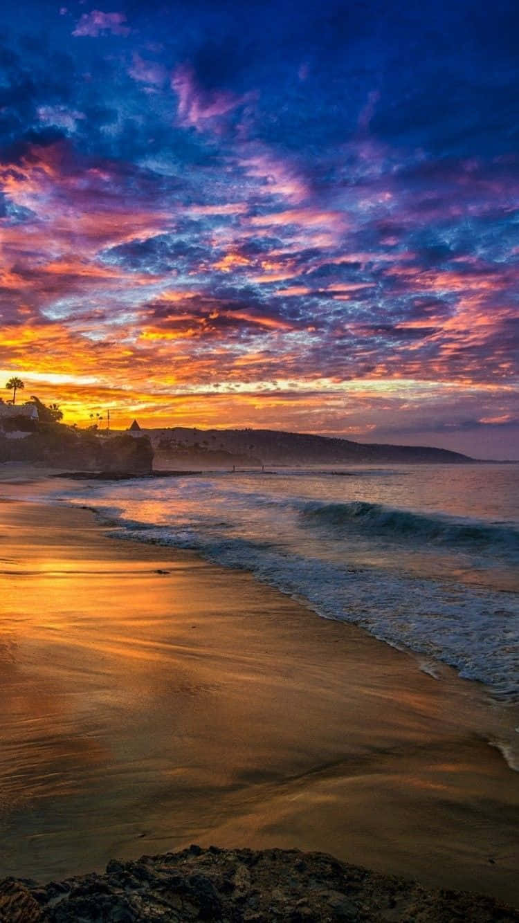 Sunset Beach iPhone 桌布 壁紙 — 夕陽西下，絢麗的色彩將天空染成火熱的橙色和深紫色，映照在平靜的海灘和溫柔的海浪之上。
