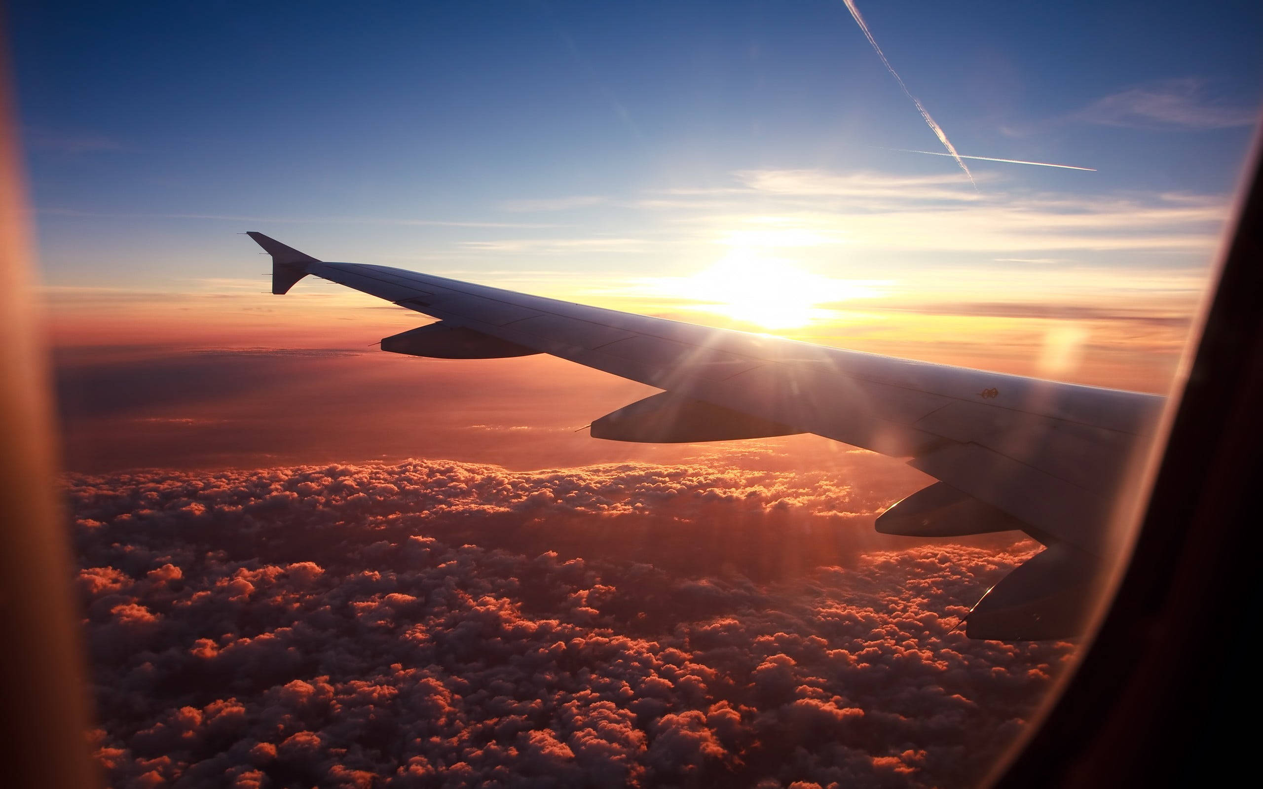 HD Plane 桌布 壁紙 — 夕陽透過飛機窗戶發光，照亮下方的雲層，機翼橫跨畫面。