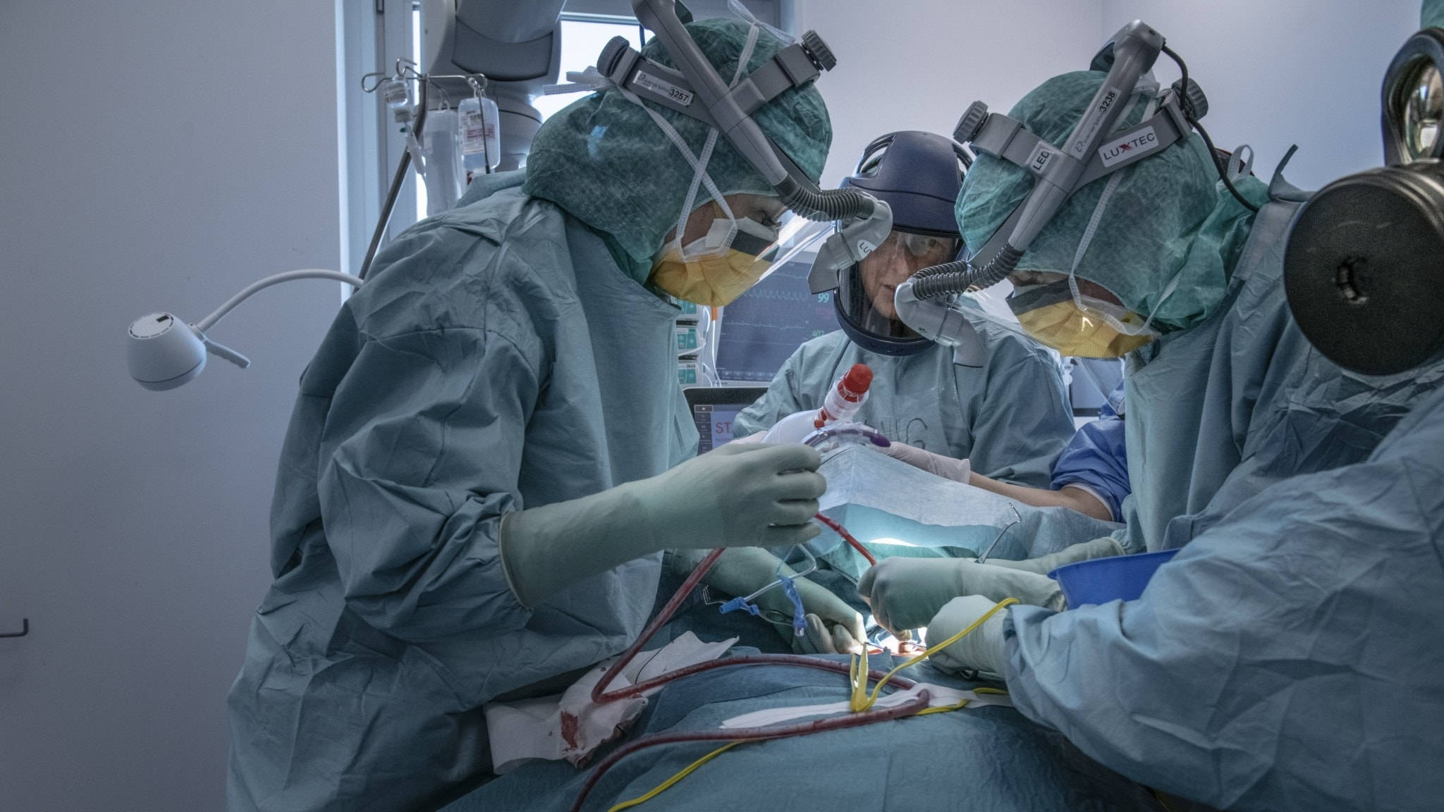 Surgeon 桌布 壁紙 — 外科醫生穿著無菌手術袍和口罩，在現代化手術室明亮的手術燈下進行精細手術。