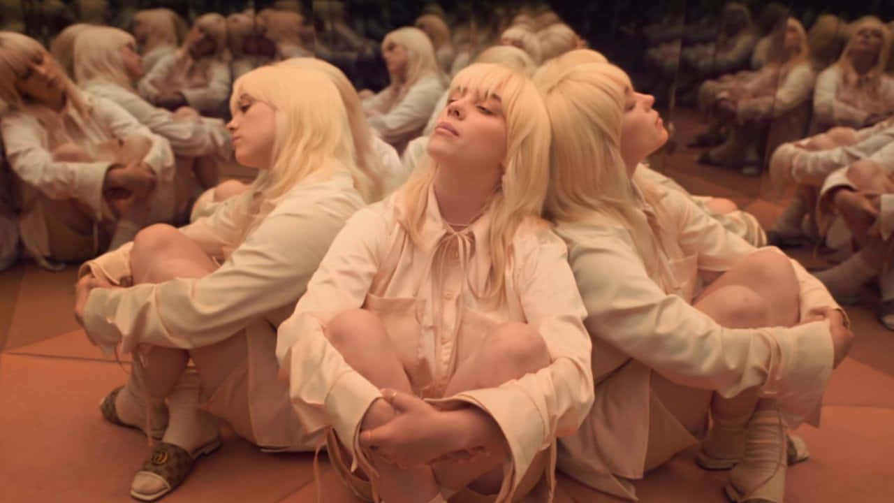 Billie Eilish Laptop 桌布 壁紙 — 多個身穿米色服裝的相同金髮女性在昏暗的鏡面牆壁房間中，盤腿坐在赤陶地板上。