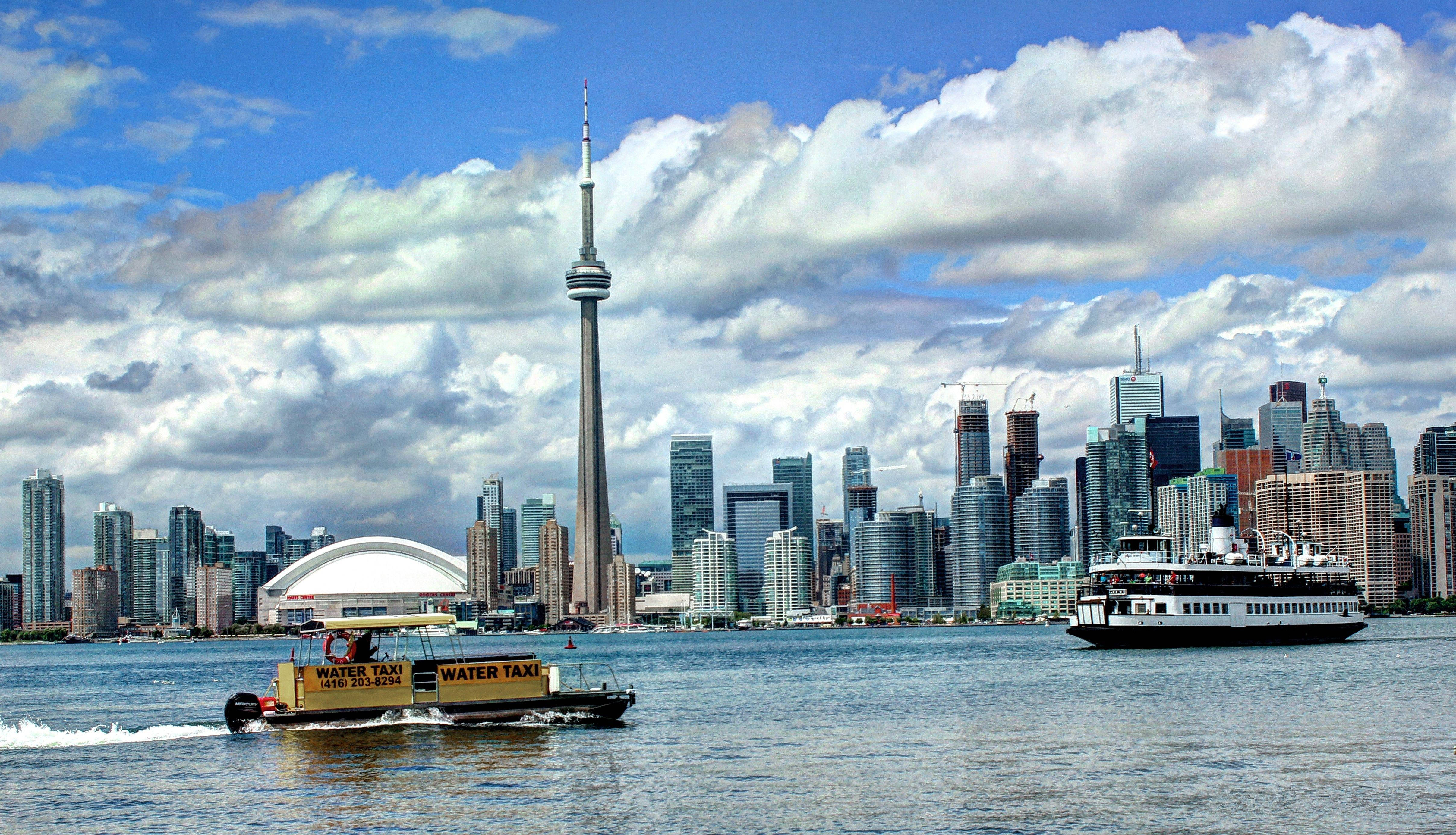 Ontario 桌布 壁紙 — 多倫多充滿活力的城市景觀，CN 塔和現代摩天大樓倒映在水中，水上計程車在部分多雲的天空下滑過海港。