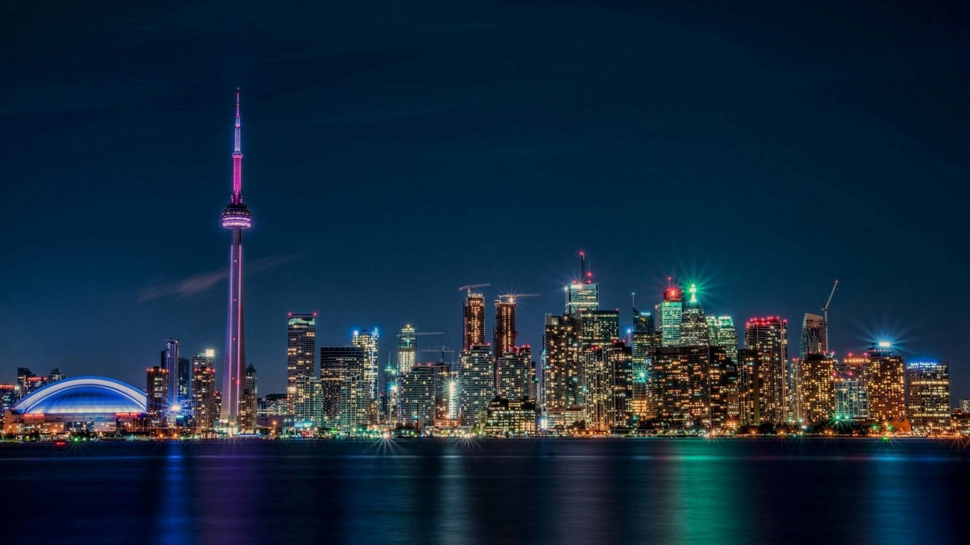 Ontario 桌布 壁紙 — 多倫多充滿活力的夜晚天際線在深藍色天空下，平靜的水面上反射出五彩繽紛的燈光。