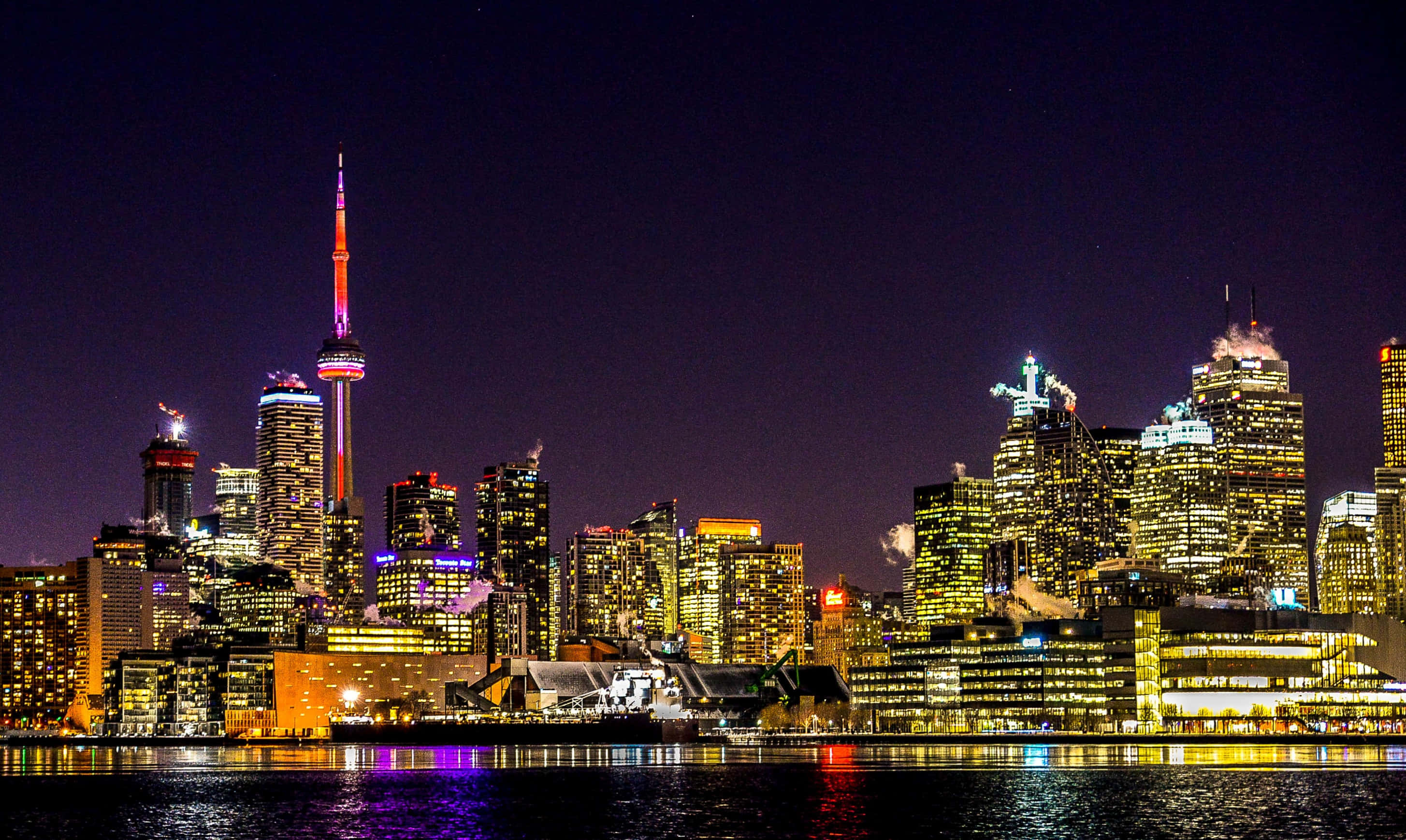 Toronto Skyline 桌布 壁紙 — 多倫多夜晚璀璨的天際線，CN塔在漆黑的天空中閃耀，倒映在平靜的水面上。