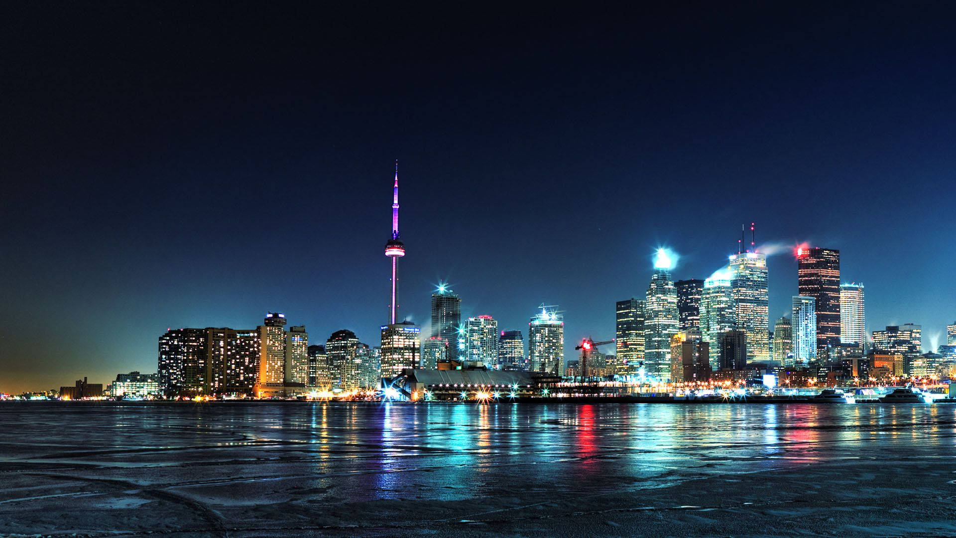 Toronto 桌布 壁紙 — 多倫多夜晚璀璨的天際線在深藍色天空下，倒映在黑暗冰冷的濱水區。