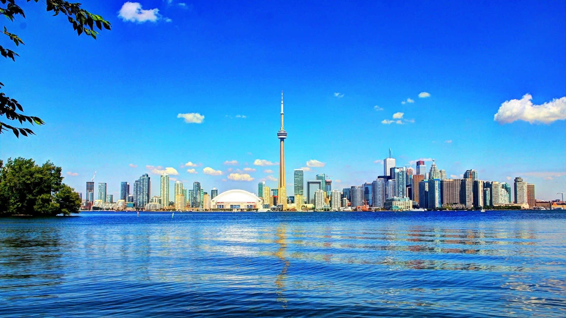 Toronto Skyline 桌布 壁紙 — 多倫多天際線，CN塔倒映在平靜的藍色水面上，天空晴朗明亮，白雲點綴。