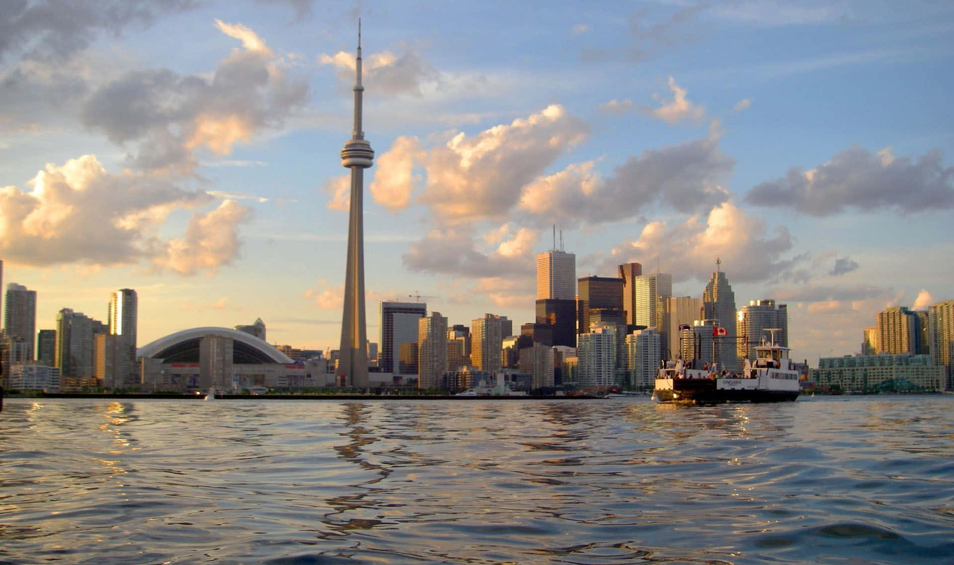 Toronto 桌布 壁紙 — 多倫多天際線在日落時分，CN塔和摩天大樓倒映在漣漪的水面上，一艘渡輪駛過。