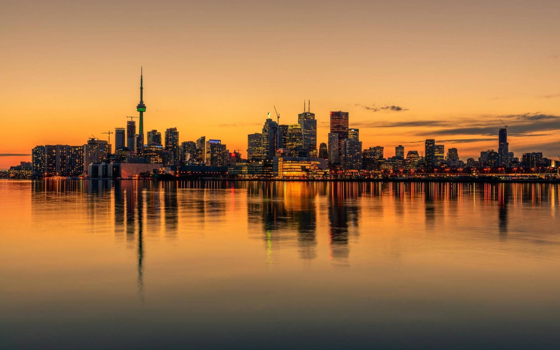 Toronto 桌布 壁紙 — 多倫多天際線在日落時分，金色燈光倒映在平靜的水面上。