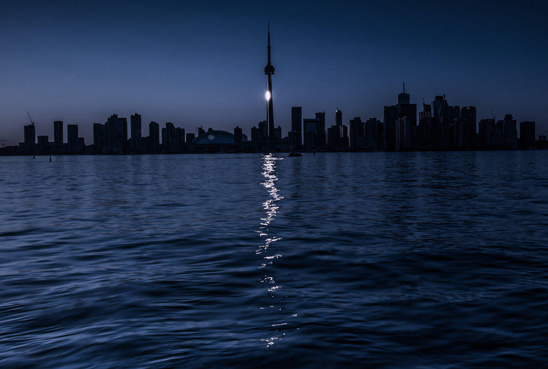 Ontario 桌布 壁紙 — 多倫多天際線在暮色中倒映在黑暗的水面上，CN塔在深藍色的天空中閃耀，呈現出一片寧靜的景色。