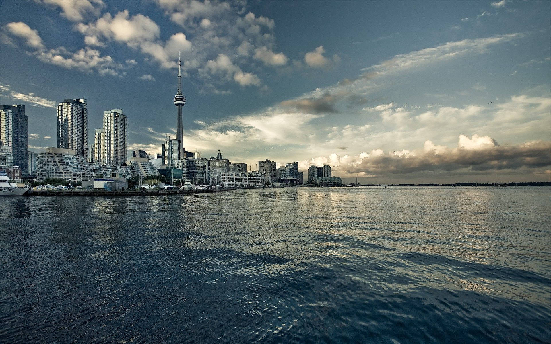 Ontario 桌布 壁紙 — 多倫多天際線的全景，CN塔在現代摩天大樓之上聳立，倒映在漣漪的水面上，天空戲劇性多雲。