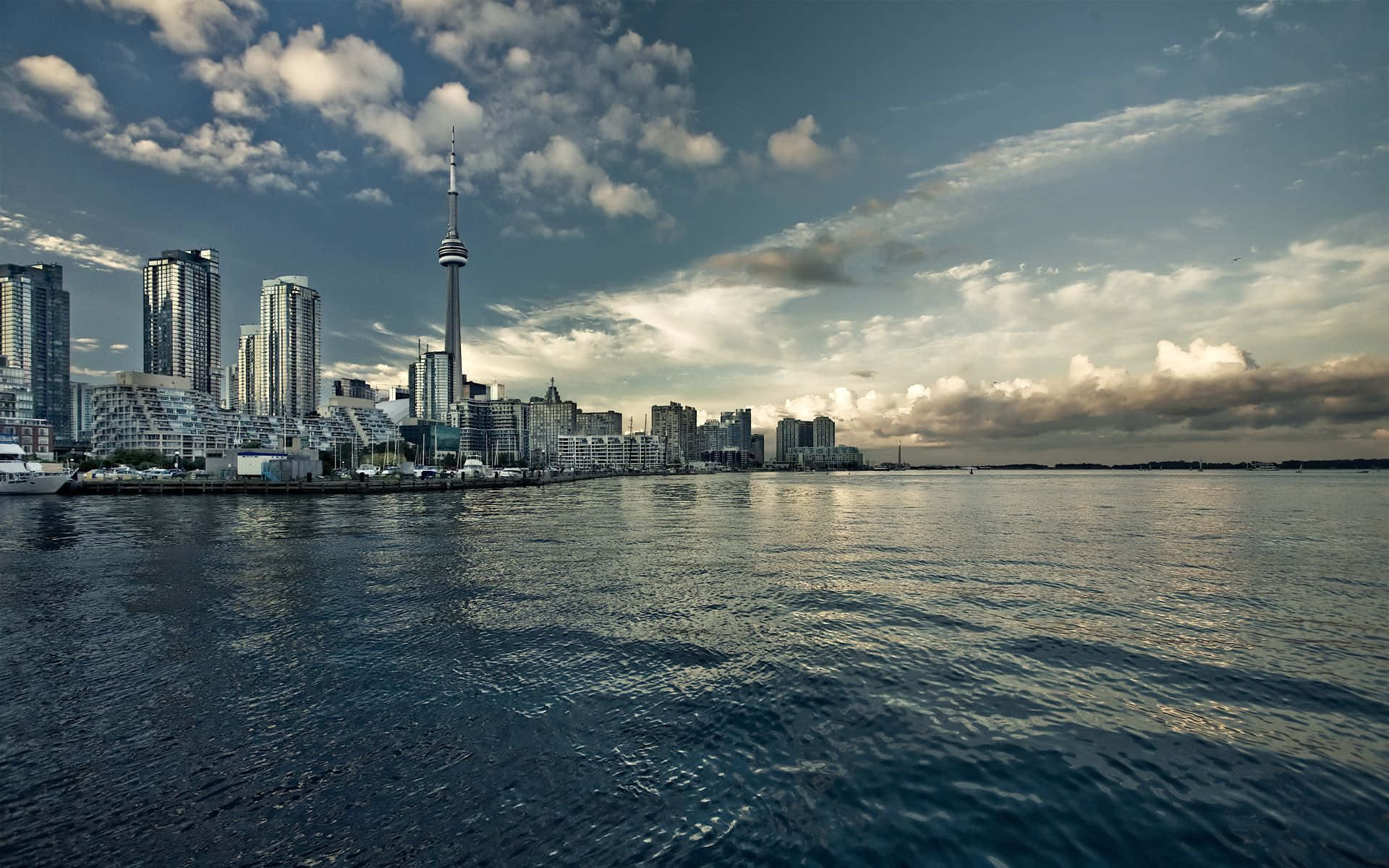 Toronto 桌布 壁紙 — 多倫多天際線的全景，CN塔在現代摩天大樓之上聳立，倒映在平靜的水面上，天空戲劇性地多雲。