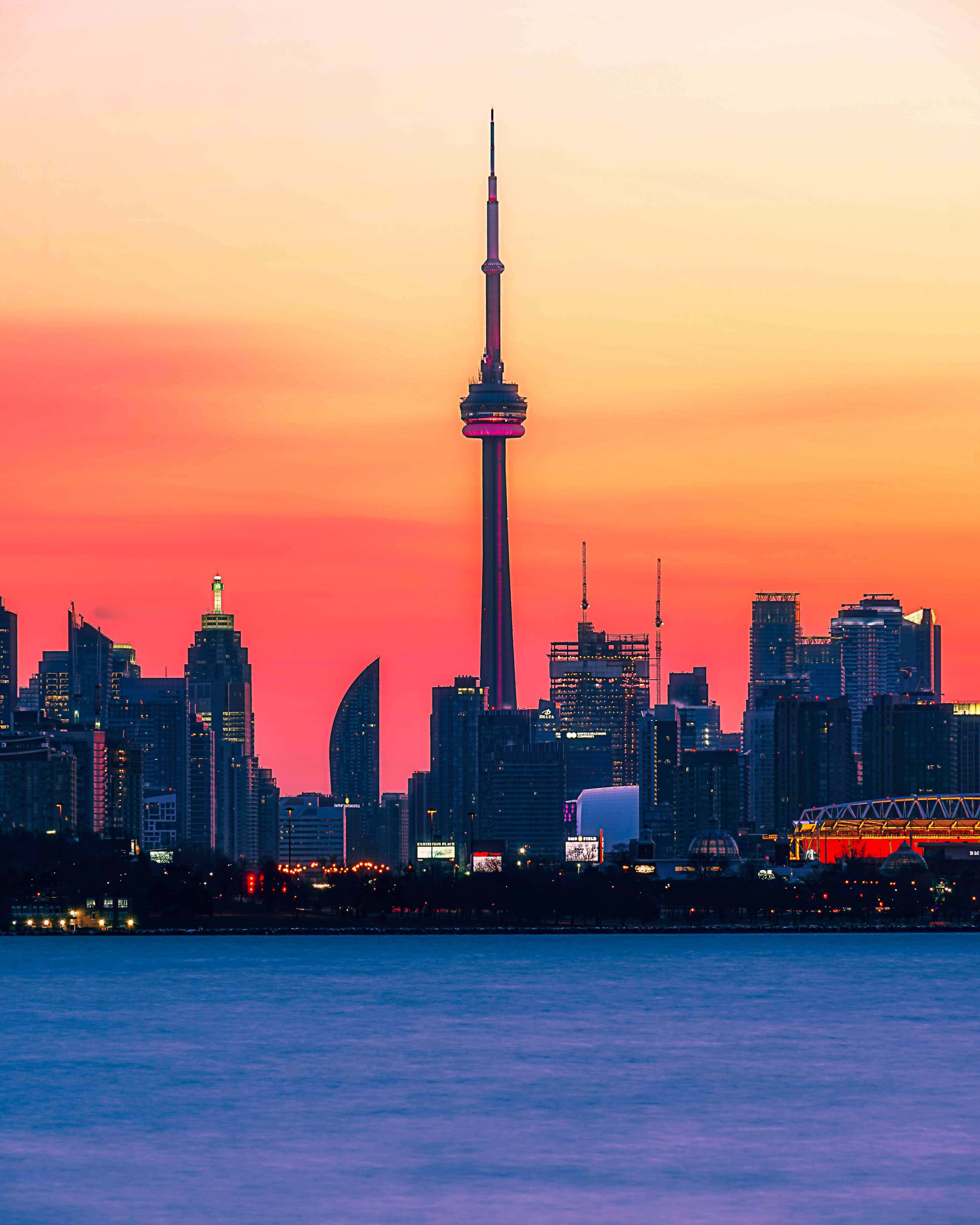 Toronto Skyline 桌布 壁紙 — 多倫多日落時分天際線，CN塔在火橙色和粉紅色雲彩映襯下閃耀，倒映在平靜的藍色水面上。