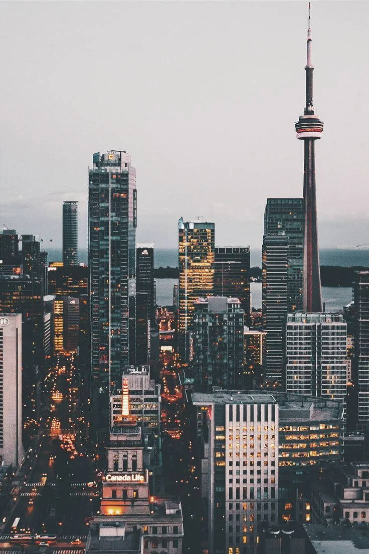 Skyscraper 桌布 壁紙 — 多倫多暮色朦朧的城市景觀，以標誌性的CN塔和發光的摩天大樓為特色，映襯著柔和的灰色天空。