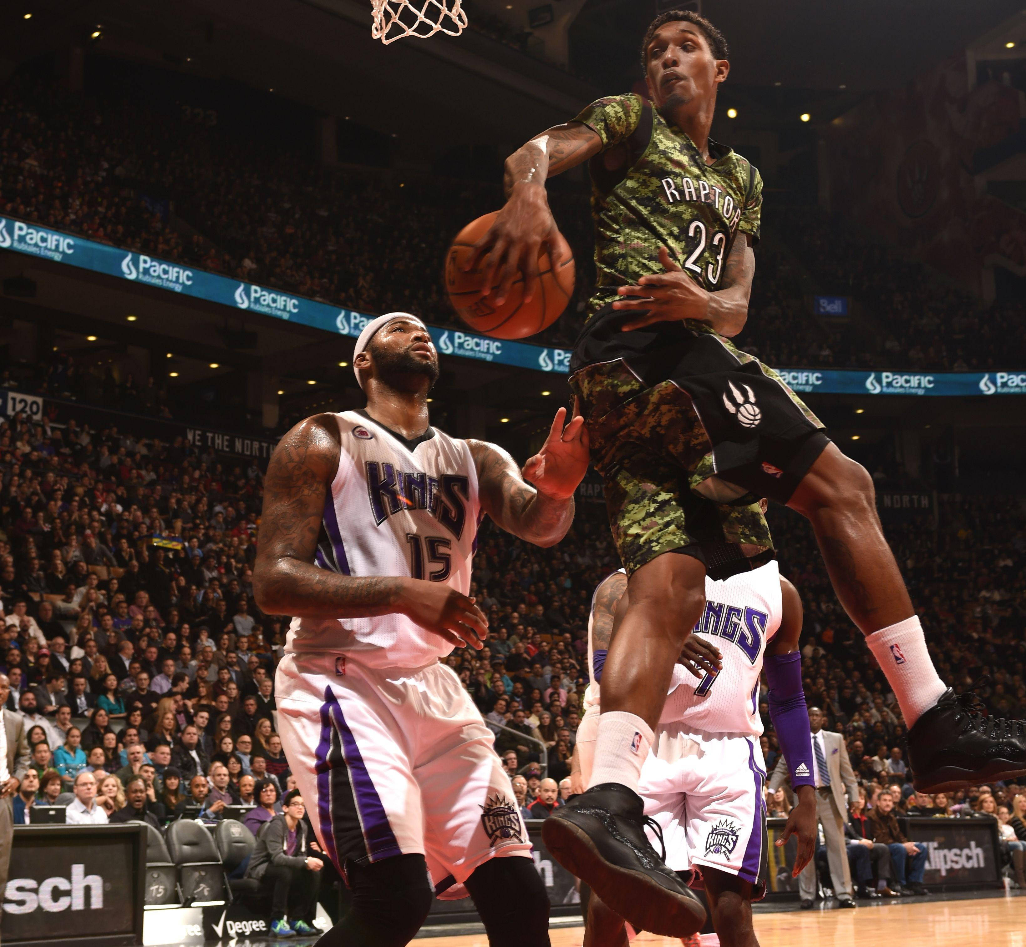 Lou Williams 桌布 壁紙 — 多倫多暴龍隊球員身穿迷彩球衣跳向籃框，而沙加緬度國王隊防守球員在座無虛席的場館比賽中起身封阻。