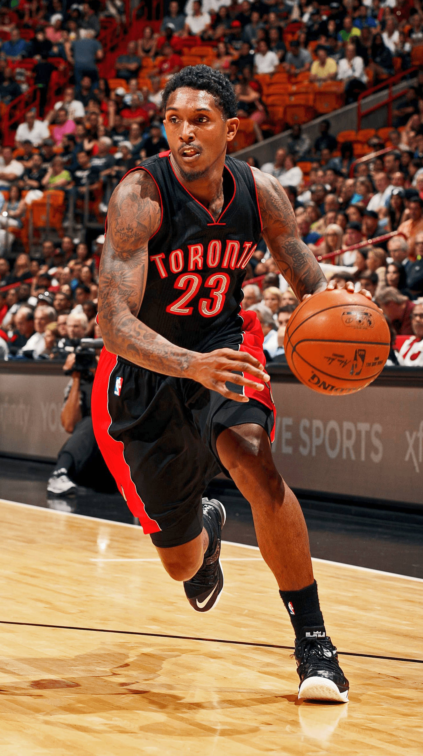 Lou Williams 桌布 壁紙 — 多倫多暴龍隊籃球運動員身穿黑色和紅色球衣，在滿場觀眾的背景下，於激烈比賽中運球。