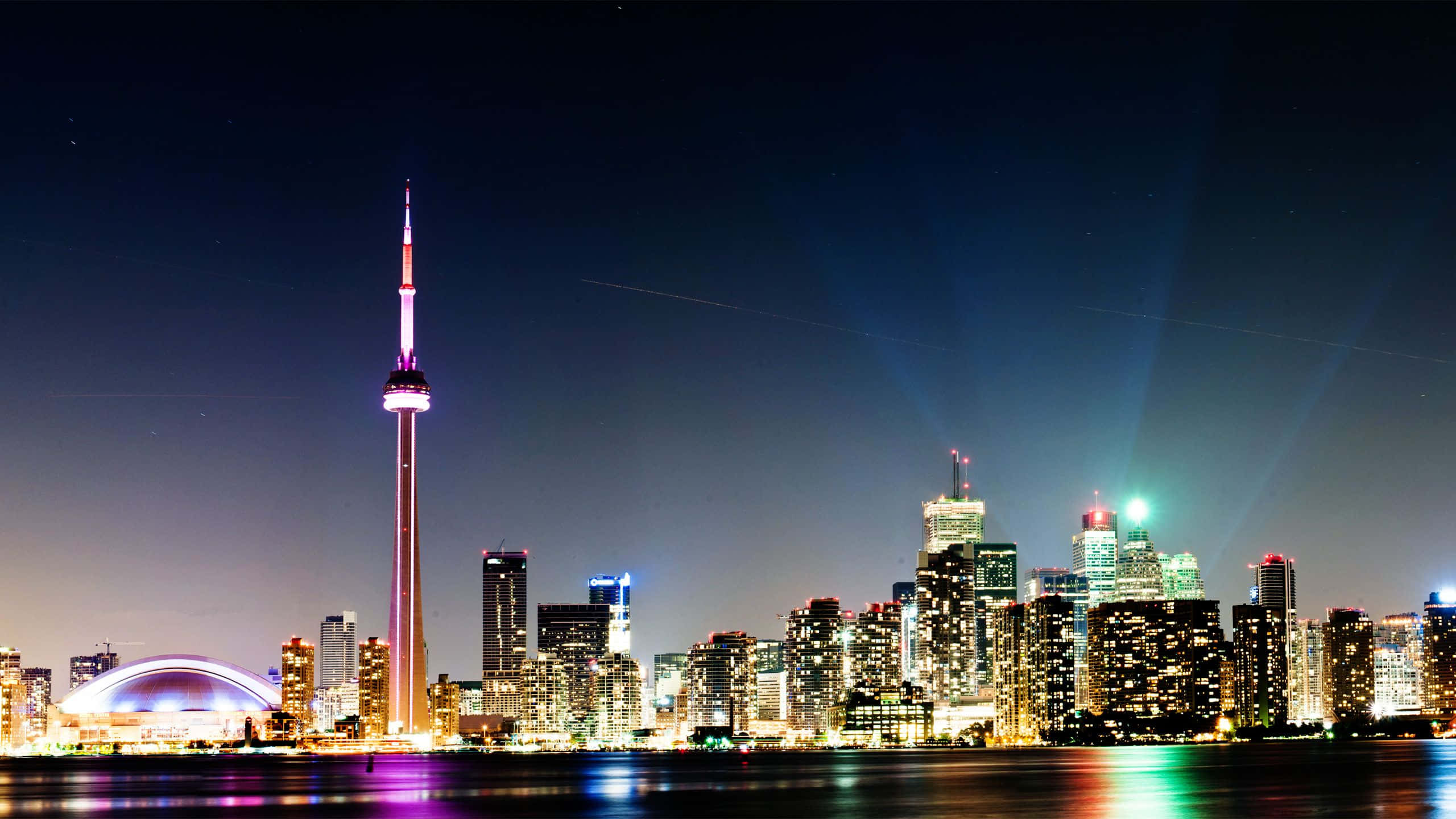 Toronto 桌布 壁紙 — 多倫多的天際線在夜晚閃耀，CN塔被紫色照亮，光束穿透黑暗的天空。