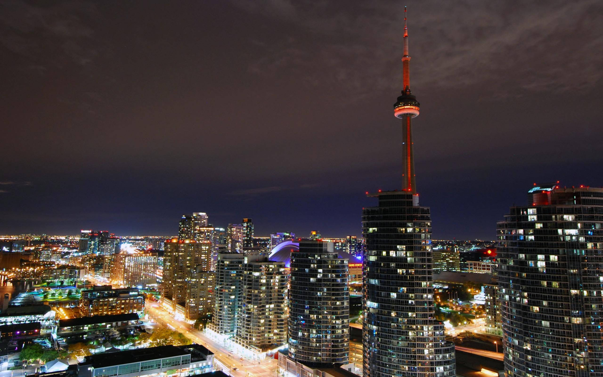 Toronto 桌布 壁紙 — 多倫多迷人的夜景，標誌性的CN塔在黑暗的天空中閃耀，下方是燈火通明的摩天大樓和街道。