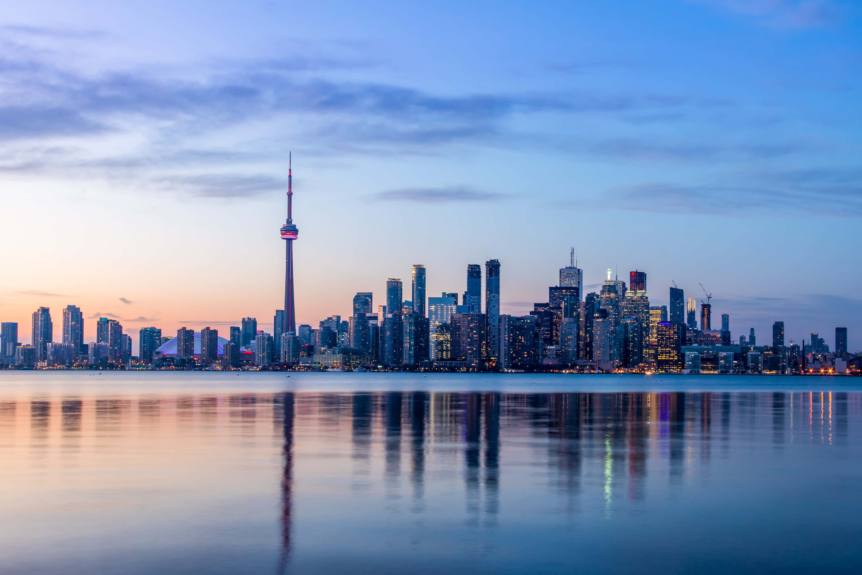 Toronto Skyline 桌布 壁紙 — 多倫多黃昏天際線，CN塔亮燈，倒映在平靜的水面上，天空呈現柔和的藍色和橙色。