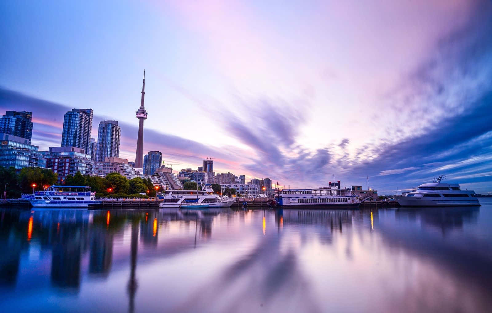 Toronto 桌布 壁紙 — 多倫多黃昏天際線，CN塔倒映在平靜的水面上，旁邊停泊著船隻，天空有紫色和藍色的雲彩。