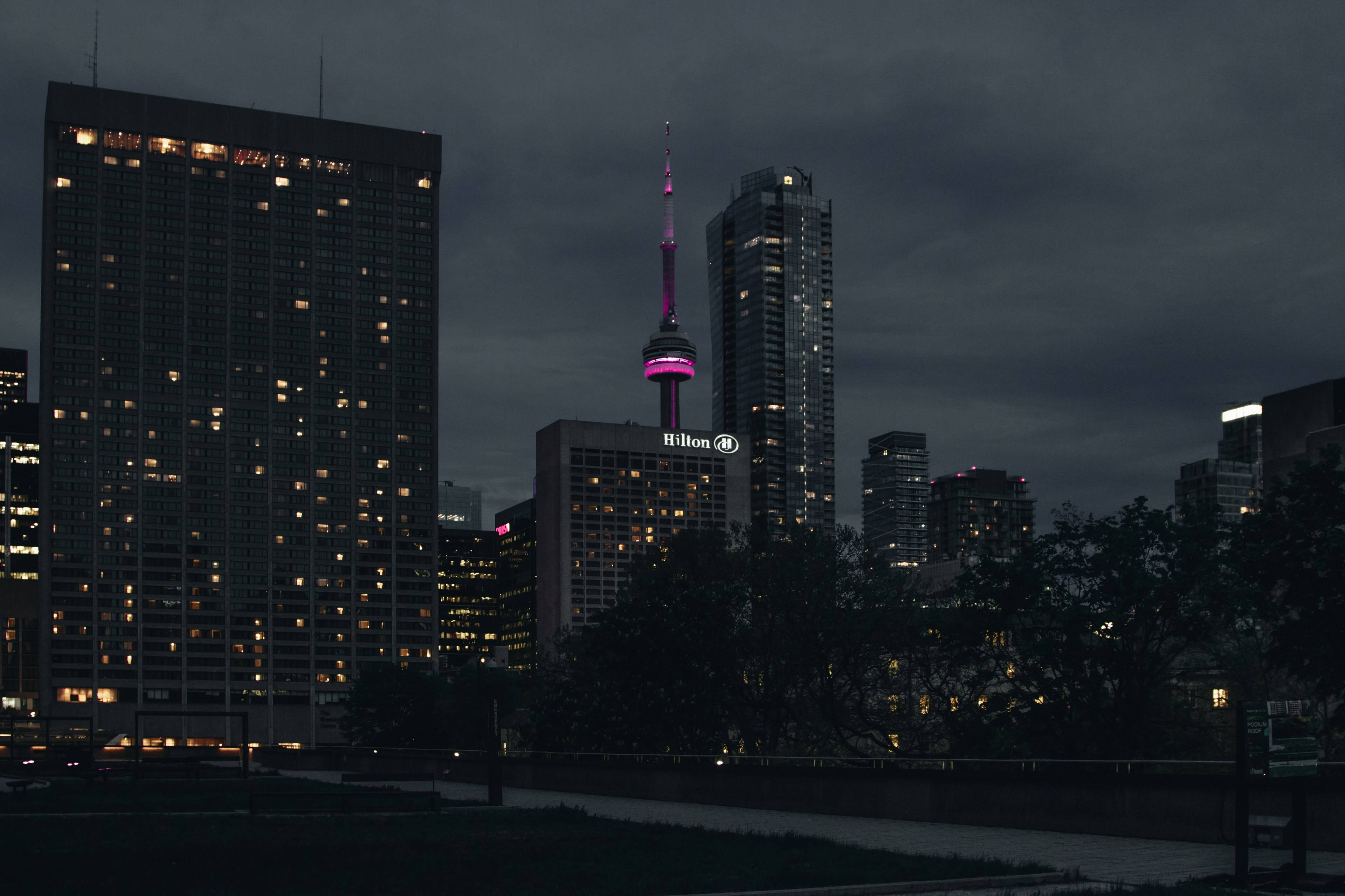 City At Night 桌布 壁紙 — 多倫多黃昏天際線，CN塔在烏雲和周圍摩天大樓亮起的窗戶映襯下閃耀著粉紅色的光芒。