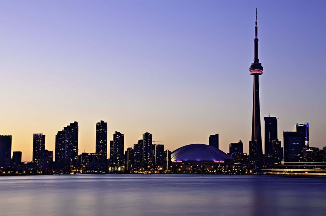 Toronto Skyline 桌布 壁紙 — 多倫多黃昏天際線，CN塔在紫色和橙色漸變的天空下亮起，倒映在平靜的水面上。