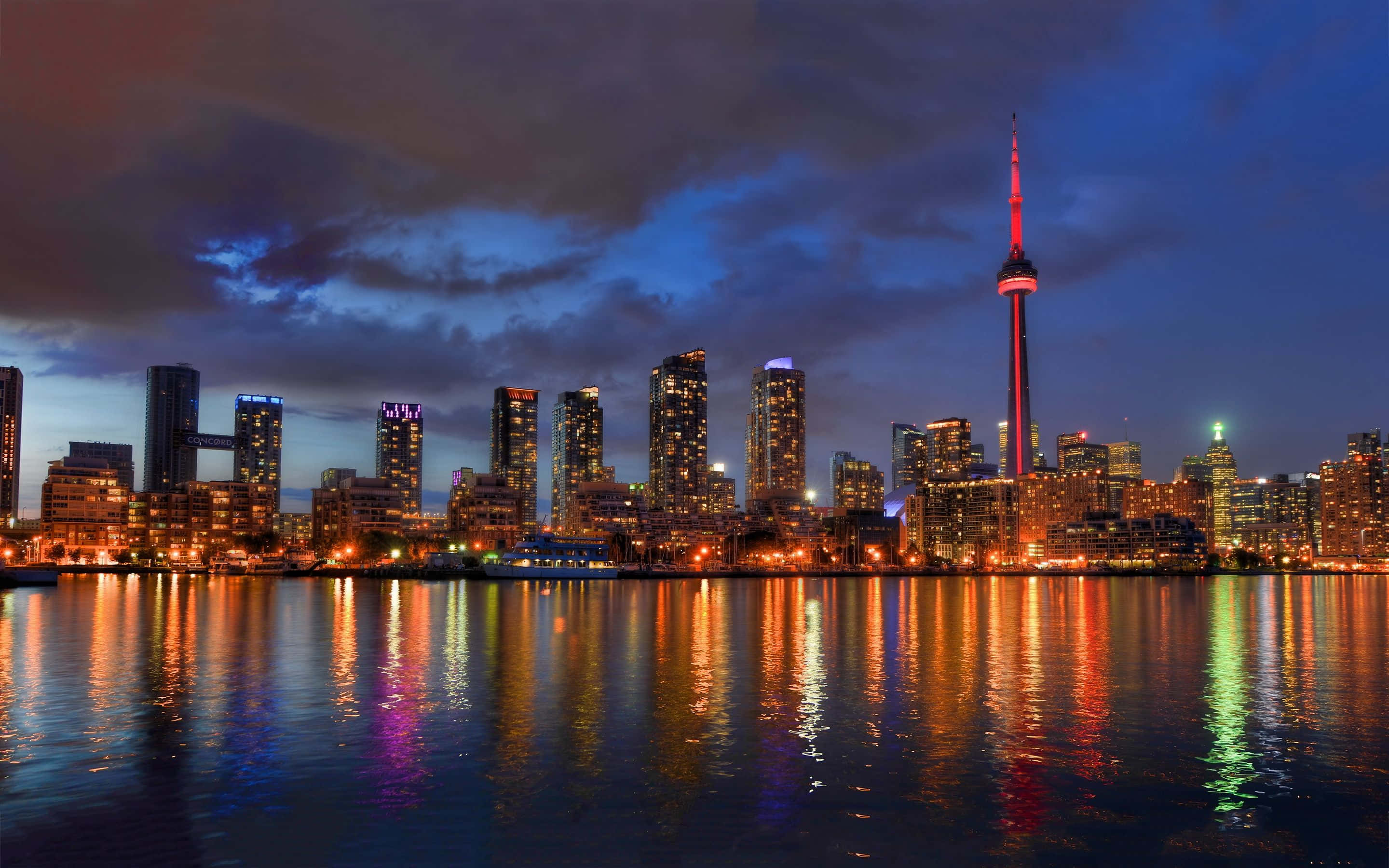 Toronto 桌布 壁紙 — 多倫多黃昏天際線，CN塔發出紅光，城市燈光在平靜的水面上倒映，天空多雲。