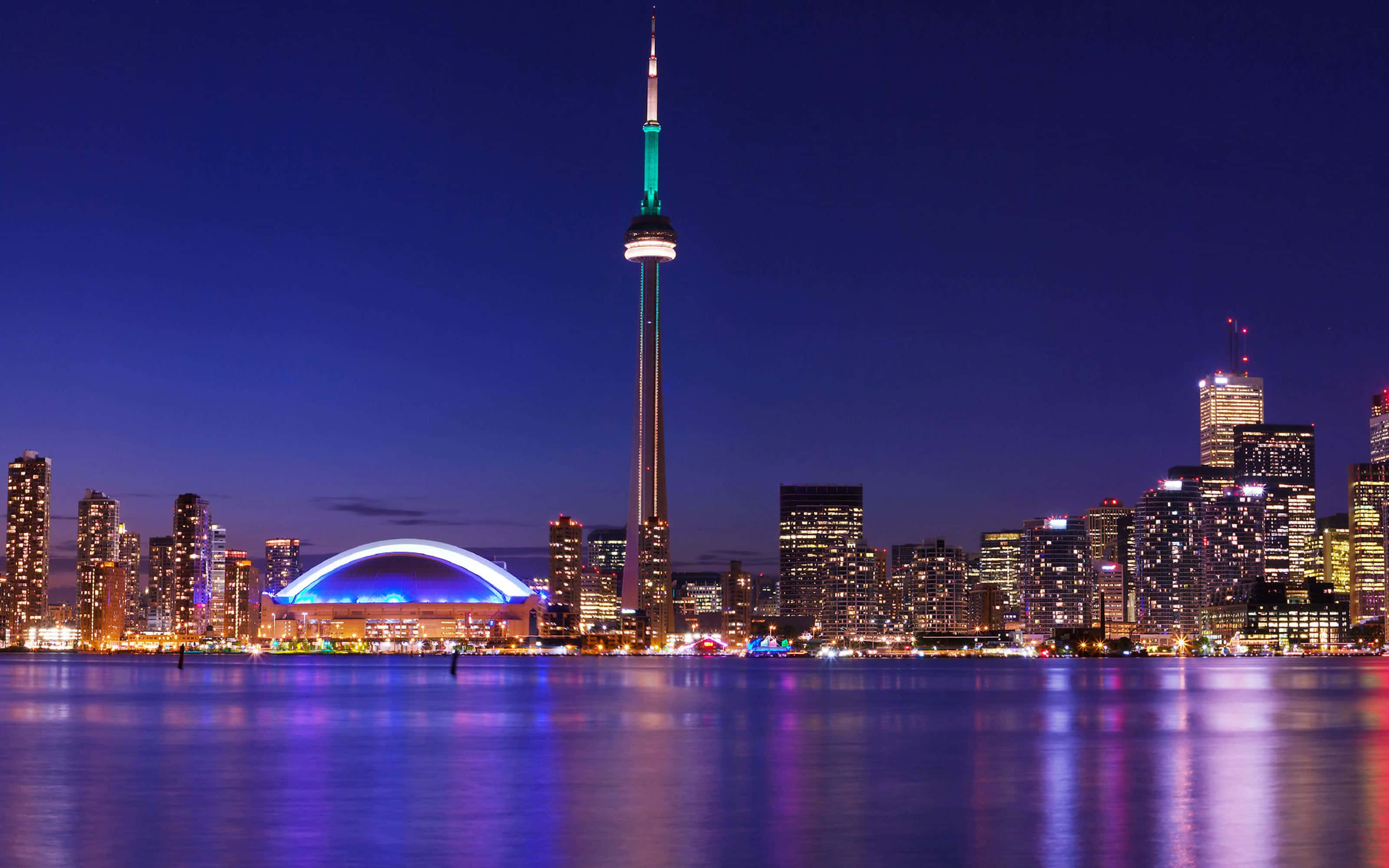 Toronto 桌布 壁紙 — 多倫多黃昏天際線，CN塔發出綠光，城市燈光倒映在平靜的水面上。