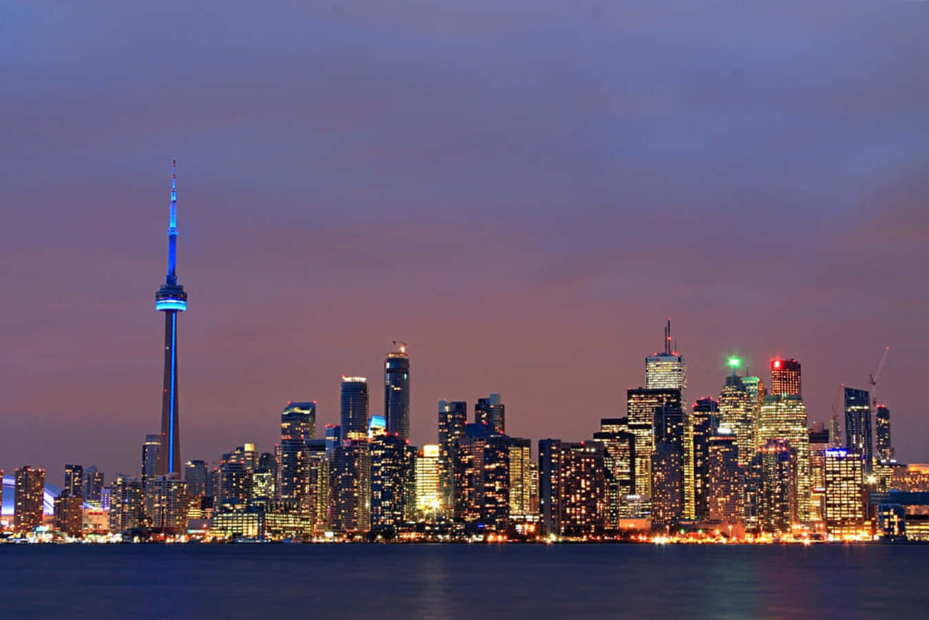 Toronto Skyline 桌布 壁紙 — 多倫多黃昏天際線，CN塔發出藍光，摩天大樓在紫色天空下亮起，倒映在平靜的水面上。