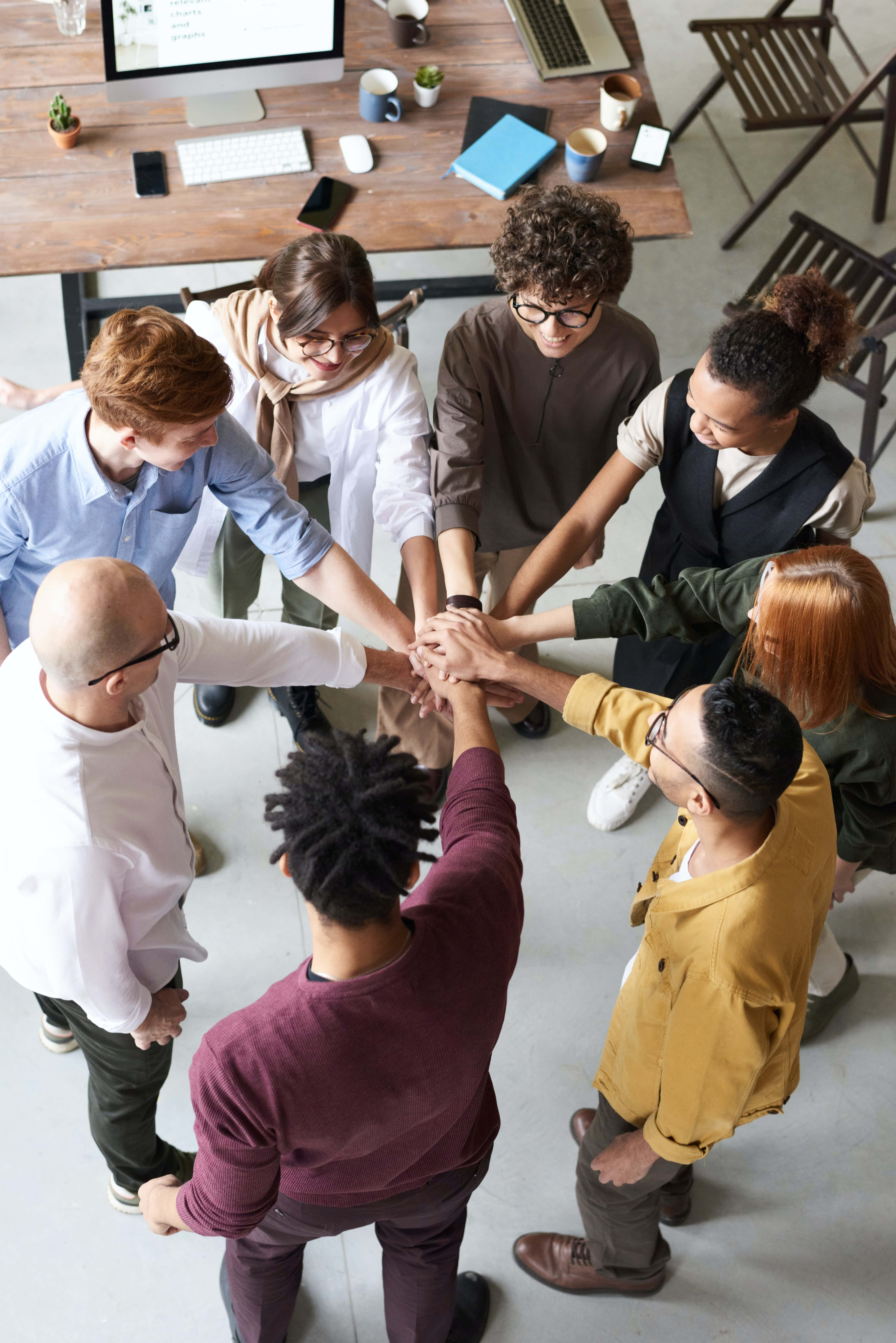 Teamwork 桌布 壁紙 — 多元化的專業團隊在現代辦公室工作空間中從上方視角疊手團結一致。